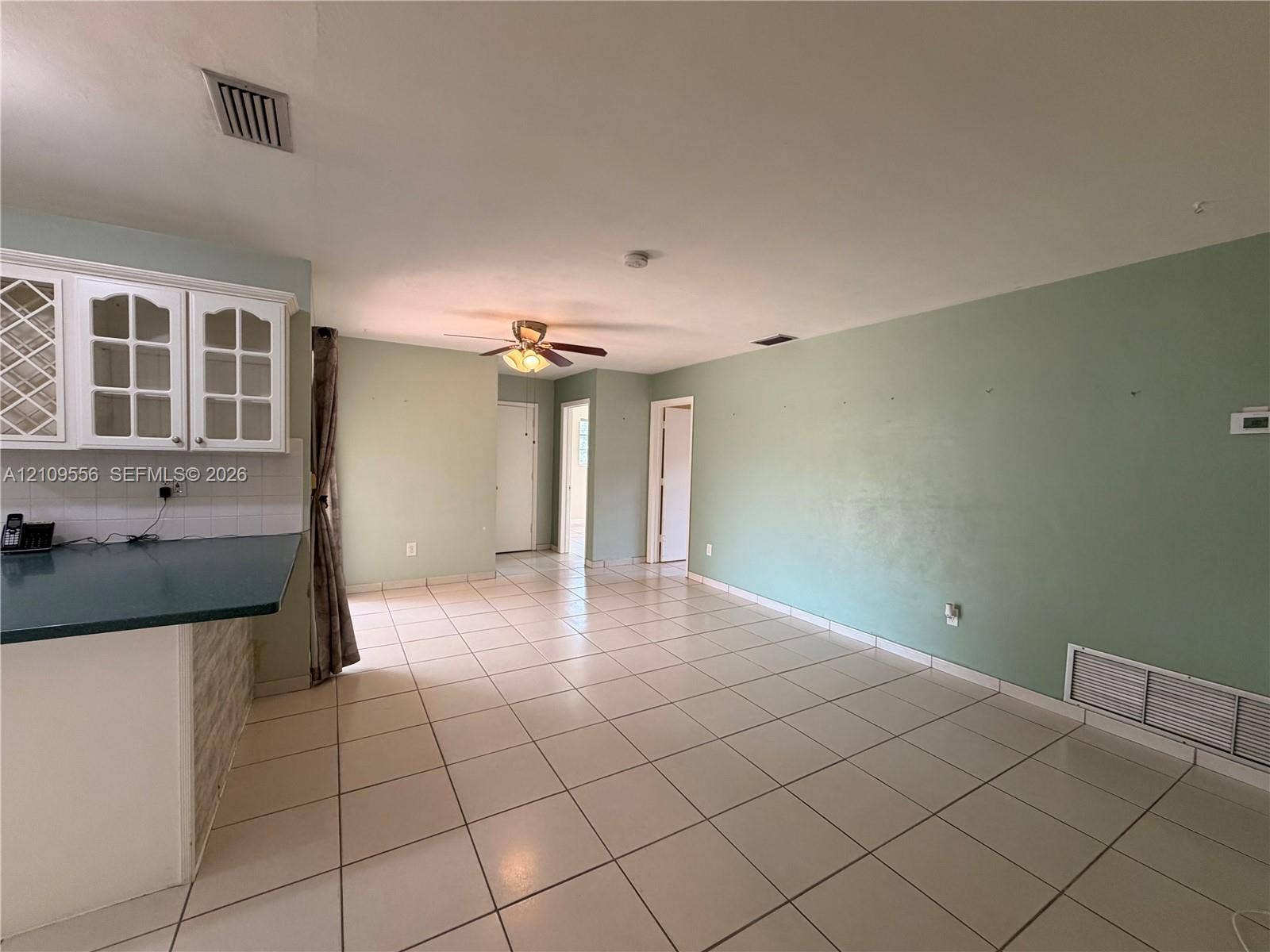 Open floor plan featuring ceramic tile flooring, kitchen cabinetry with glass-paneled uppers, a solid-surface breakfast bar, and a ceiling fan