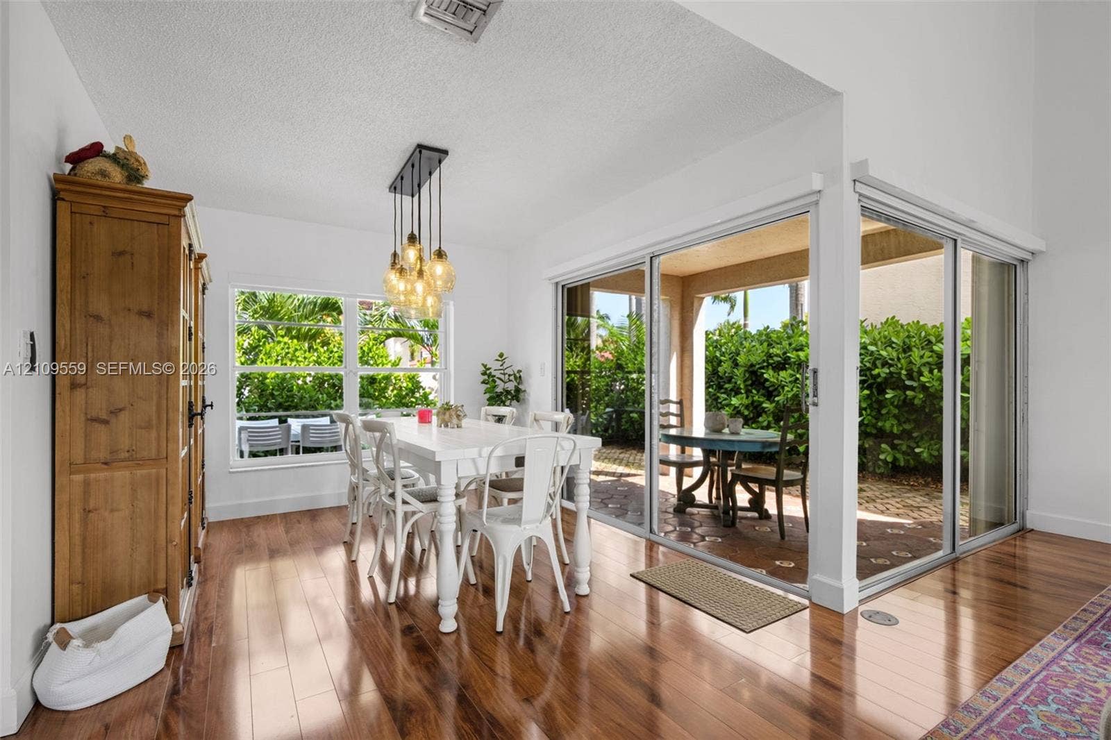 10217 NW 56th Street, Doral, FL 33178 Wood-finish flooring, multi-pane window, suspended linear light fixture, and floor-to-ceiling glass sliding doors opening to a covered patio