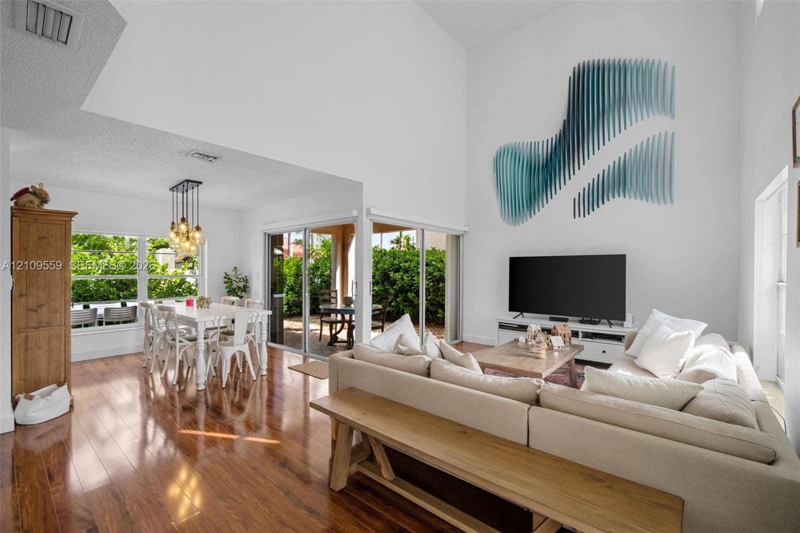 10217 NW 56th Street, Doral, FL 33178 High-ceiling living area featuring wood-finish flooring, floor-to-ceiling glass sliding doors, and multi-pendant dining room lighting