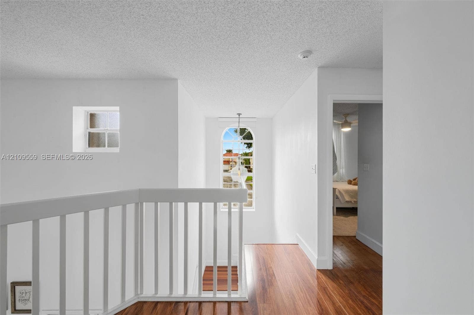 10217 NW 56th Street, Doral, FL 33178 Arched window with decorative grille, white spindle railing, wood-finish flooring, and recessed ceiling-mounted lighting