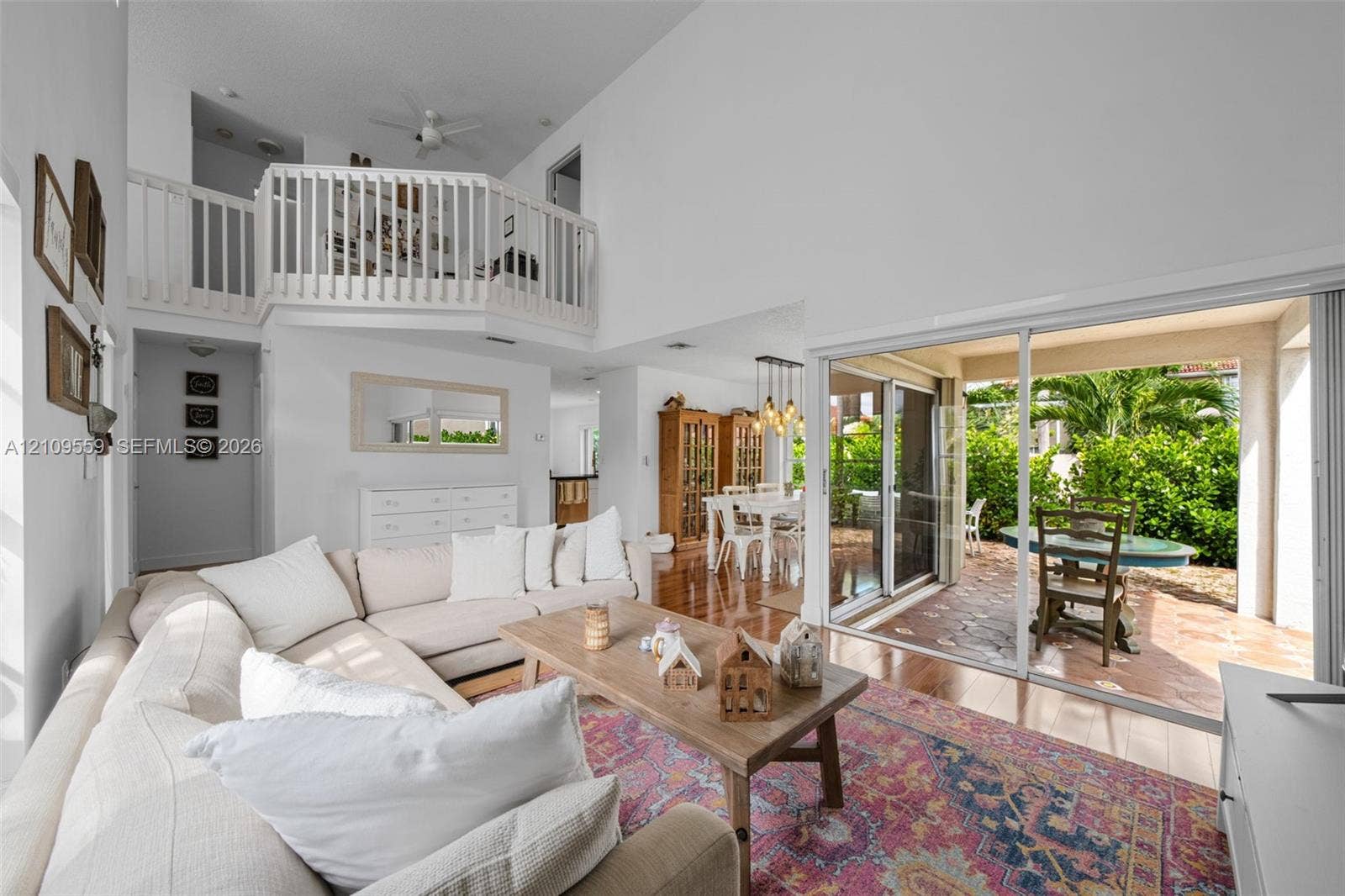 10217 NW 56th Street, Doral, FL 33178 Living area with vaulted ceilings, elevated mezzanine loft with white railing, wood-finish flooring, and large sliding glass doors opening to a tiled patio