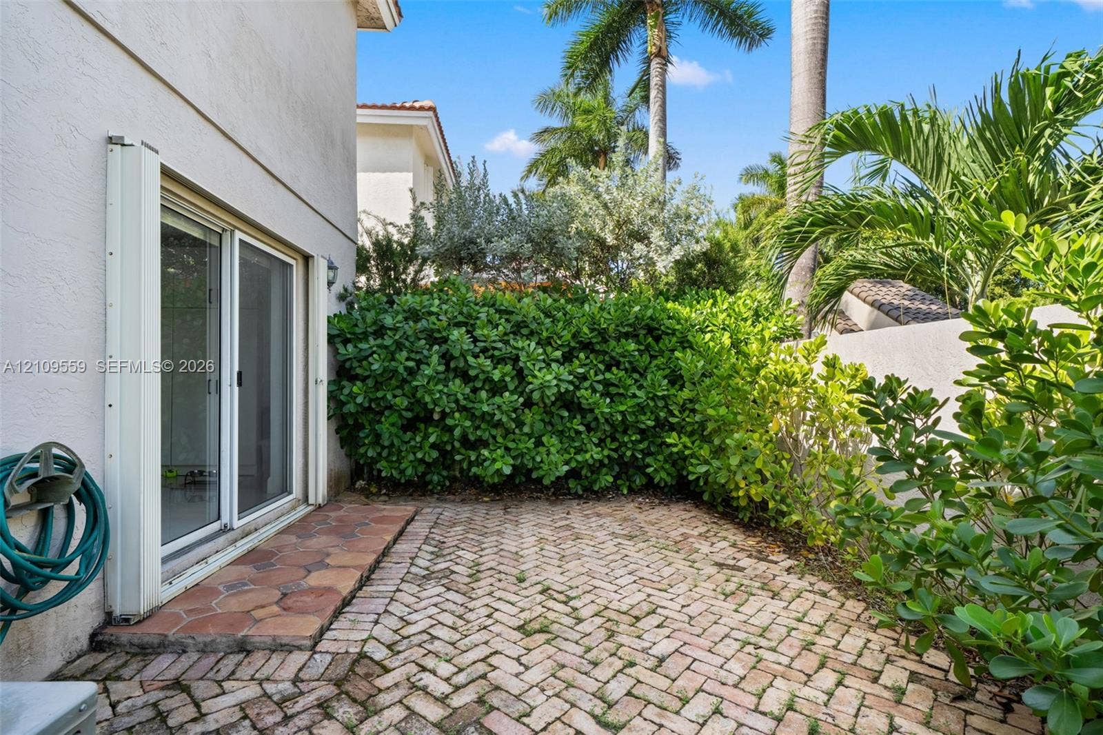 10217 NW 56th Street, Doral, FL 33178 Private patio featuring herringbone-pattern brick paving, natural stone border accents, and established hedge landscaping