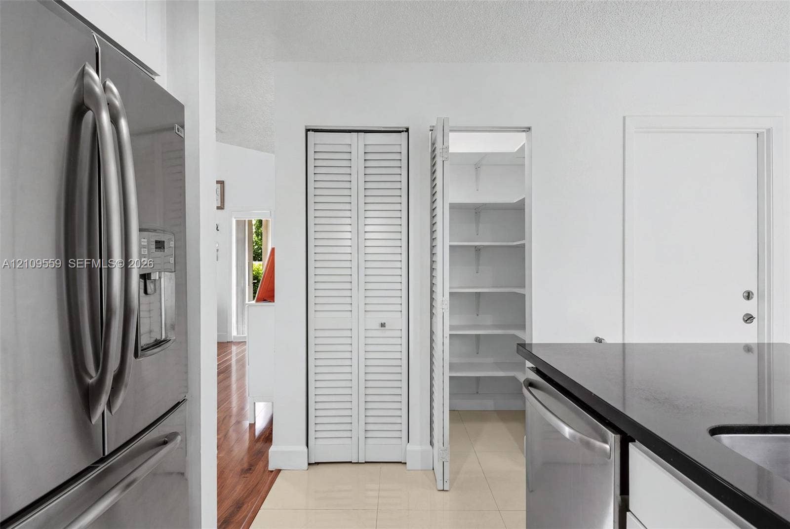10217 NW 56th Street, Doral, FL 33178 Stainless steel refrigerator, built-in pantry with white louvered doors and interior shelving, and solid-surface countertop with undermount sink