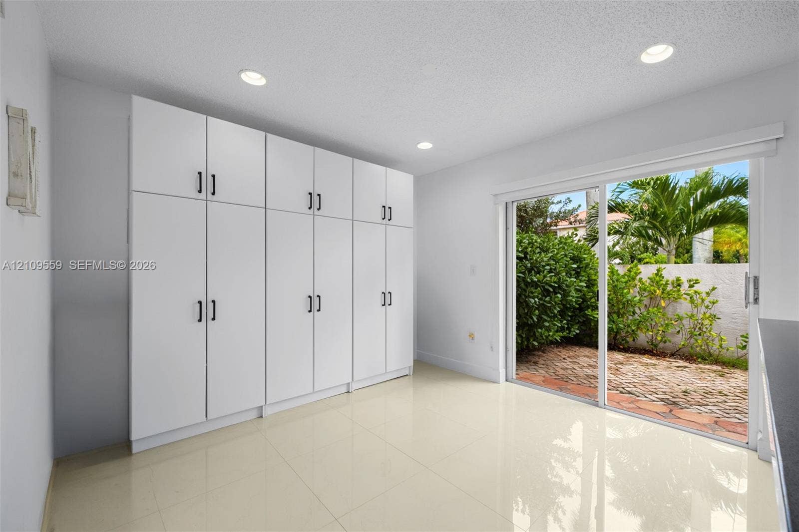 10217 NW 56th Street, Doral, FL 33178 Floor-to-ceiling white cabinetry with matte black hardware, recessed lighting, and sliding glass doors opening to a brick-paved patio