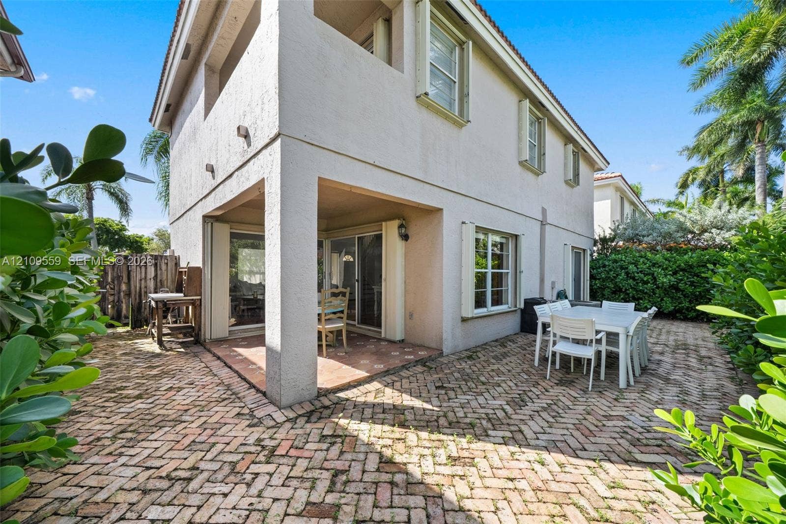 10217 NW 56th Street, Doral, FL 33178 Two-story exterior featuring a covered patio, brick-paver hardscaping, upper-level balcony, and exterior light fixtures