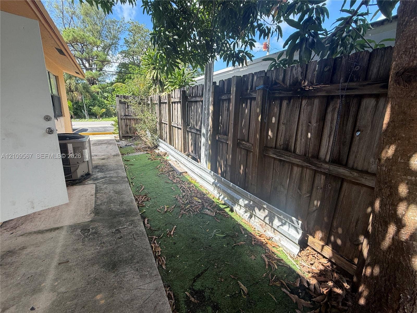 1132 NE 5th Avenue, #1, Fort Lauderdale, Fort Lauderdale, FL 33304 Exterior side yard featuring concrete hardscaping, vertical wood privacy fencing with a metal base plate, and mature trees