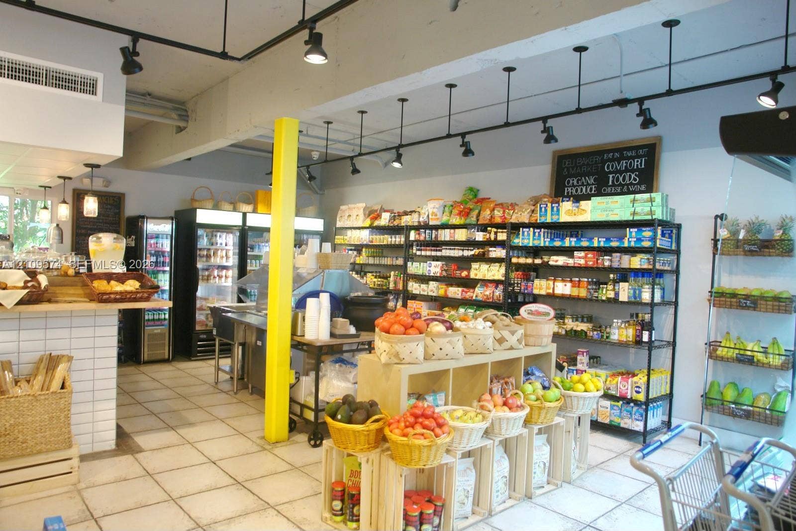 Commercial space featuring industrial-style track lighting, square tile flooring, exposed ceiling beams, built-in white tiled service counter, and floor-to-ceiling metal shelving
