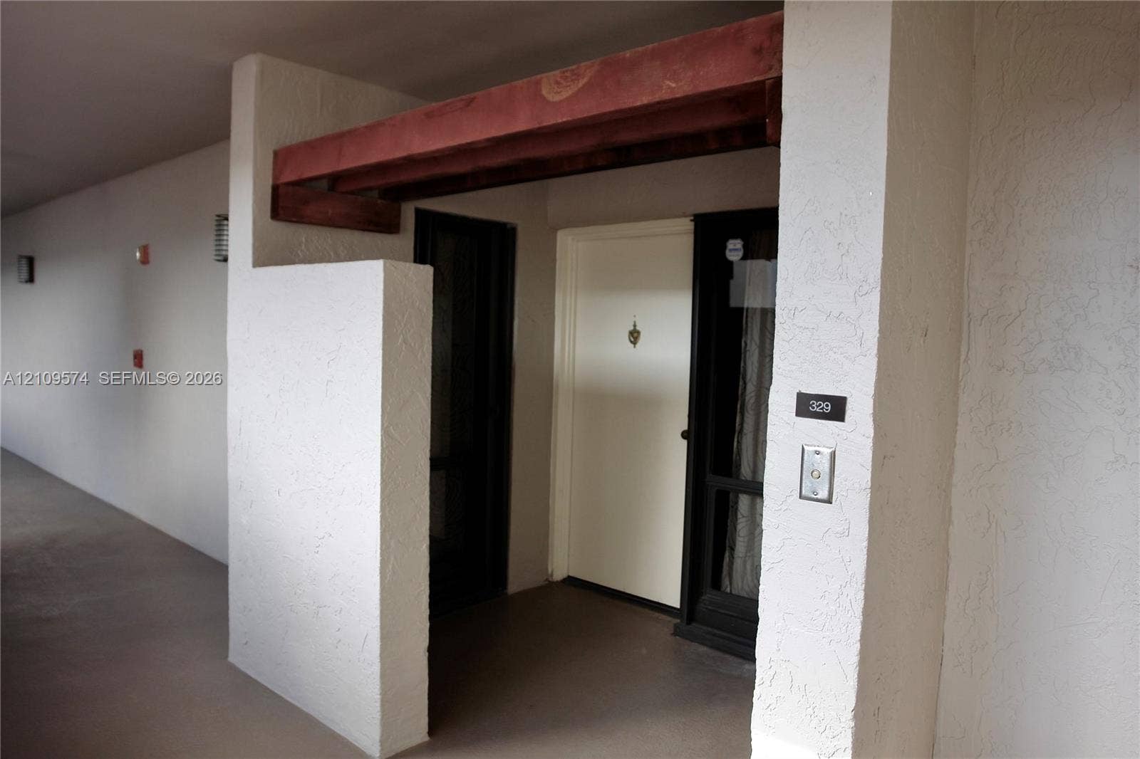 Covered entryway featuring a textured stucco facade, exposed wood beam accent, and a solid-core front door