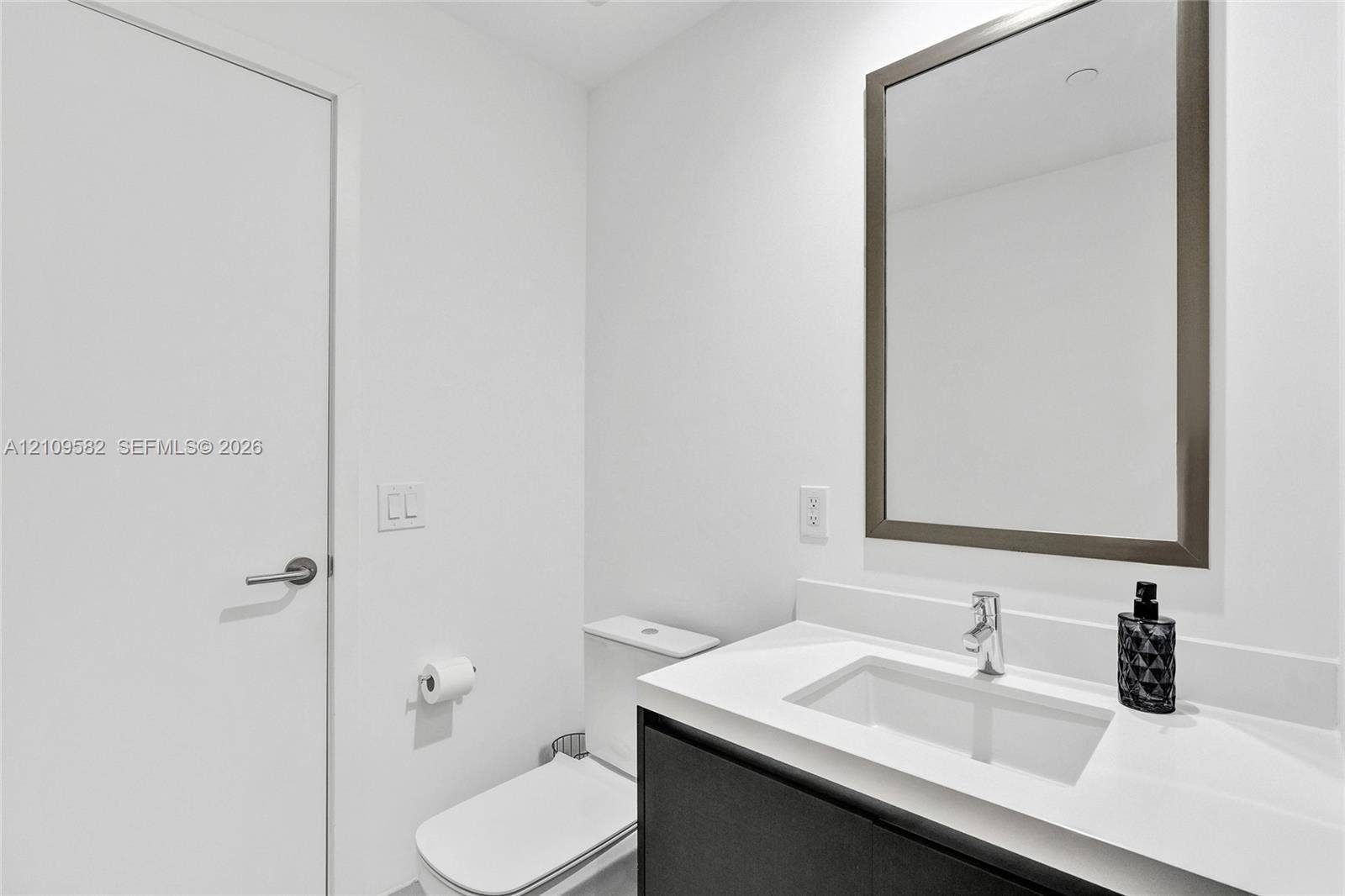 Modern vanity with a light-toned countertop, rectangular undermount sink, chrome faucet, and dark-finish base cabinetry, accompanied by a framed mirror