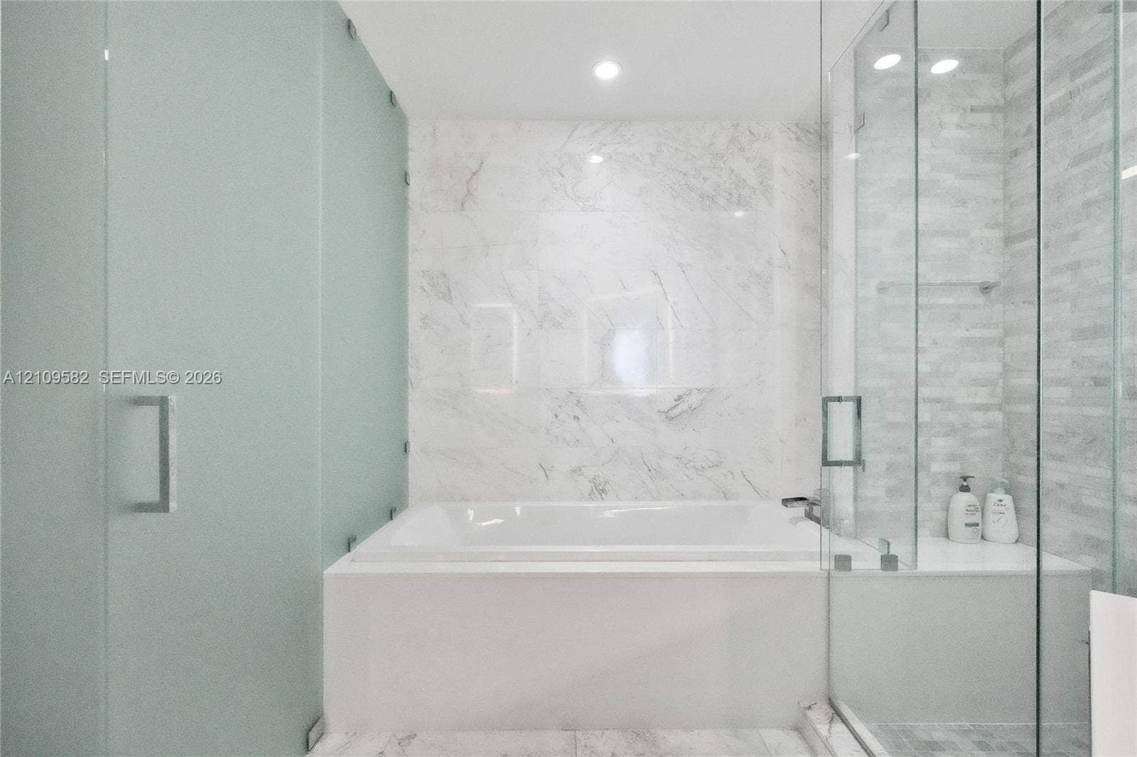 Soaking tub with stone-finish surround, glass-enclosed shower featuring tile walls, and recessed lighting