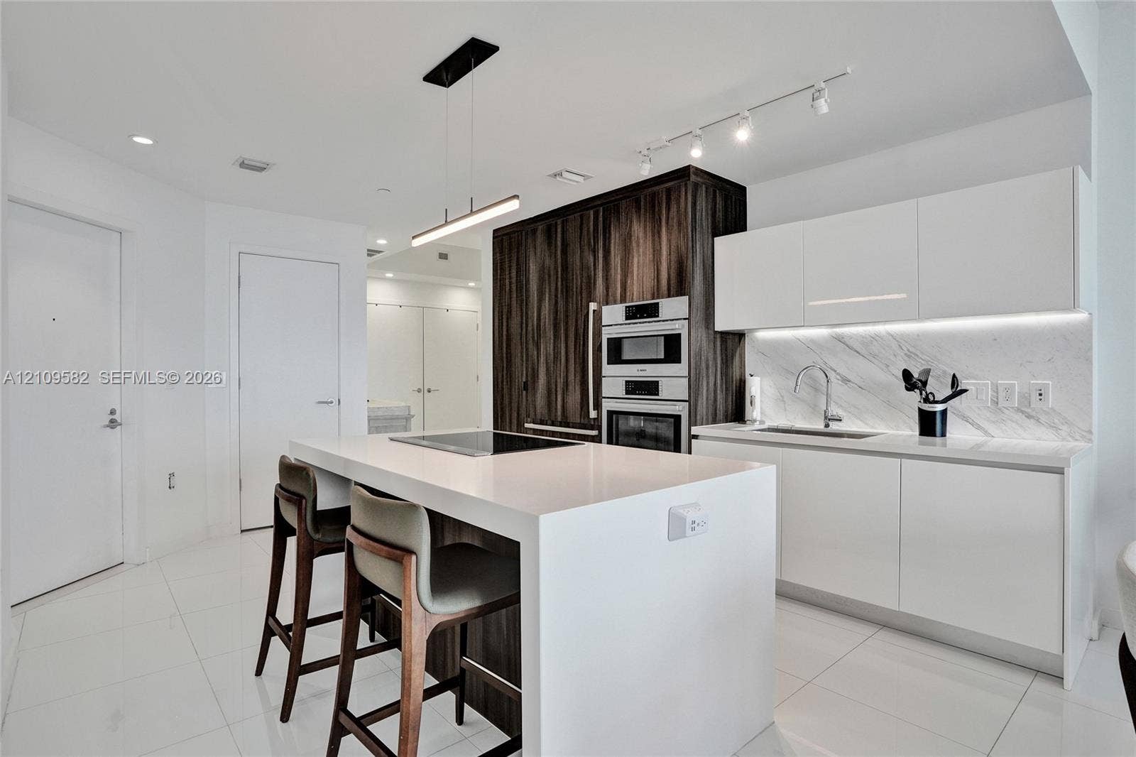 Kitchen featuring a central island with a quartz countertop, flat-panel cabinetry, a built-in wall oven and microwave, stone-finish backsplash, and integrated under-cabinet lighting