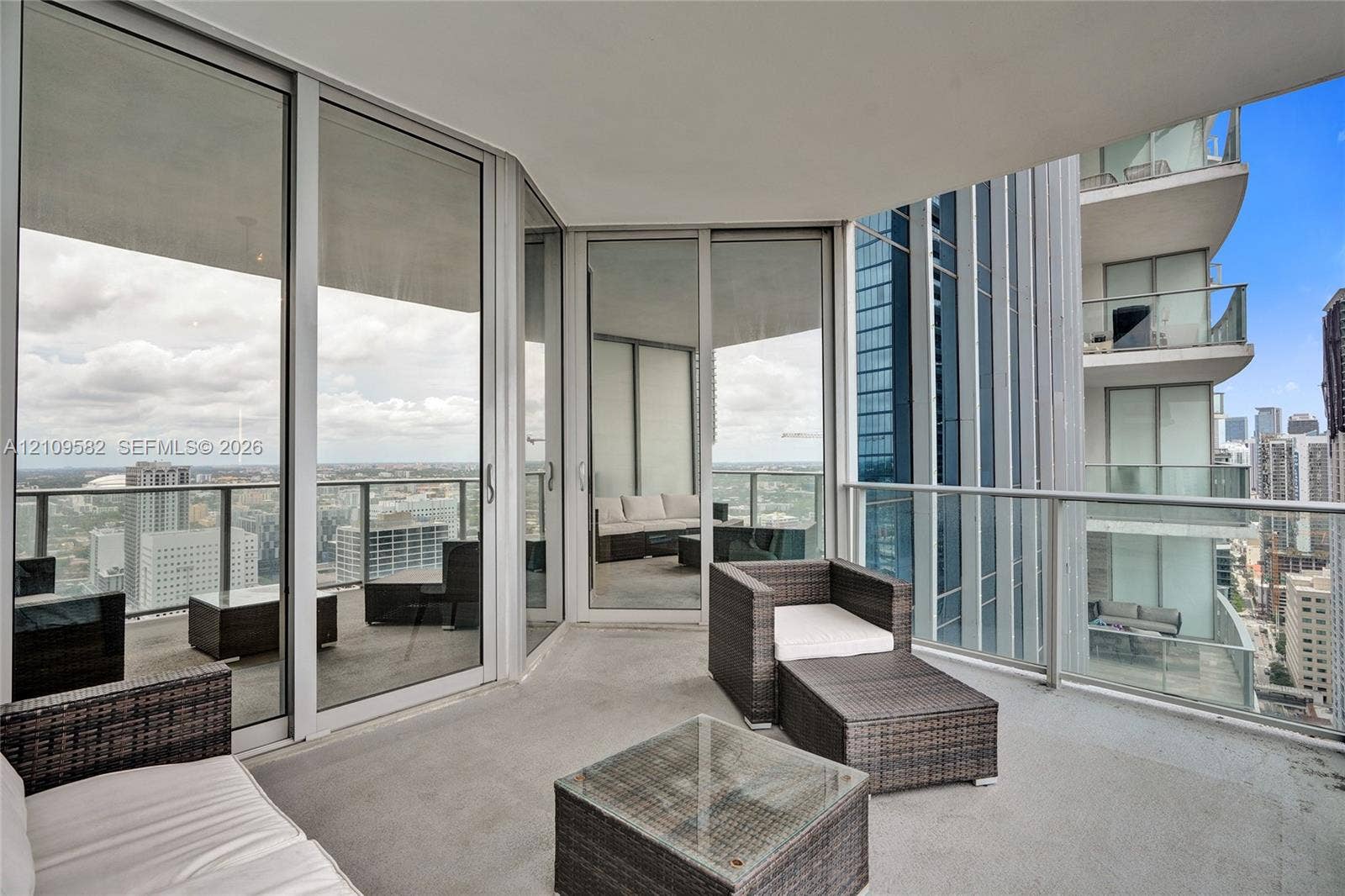 Covered wrap-around balcony with concrete flooring, full-height glass panel doors, and integrated metal railing