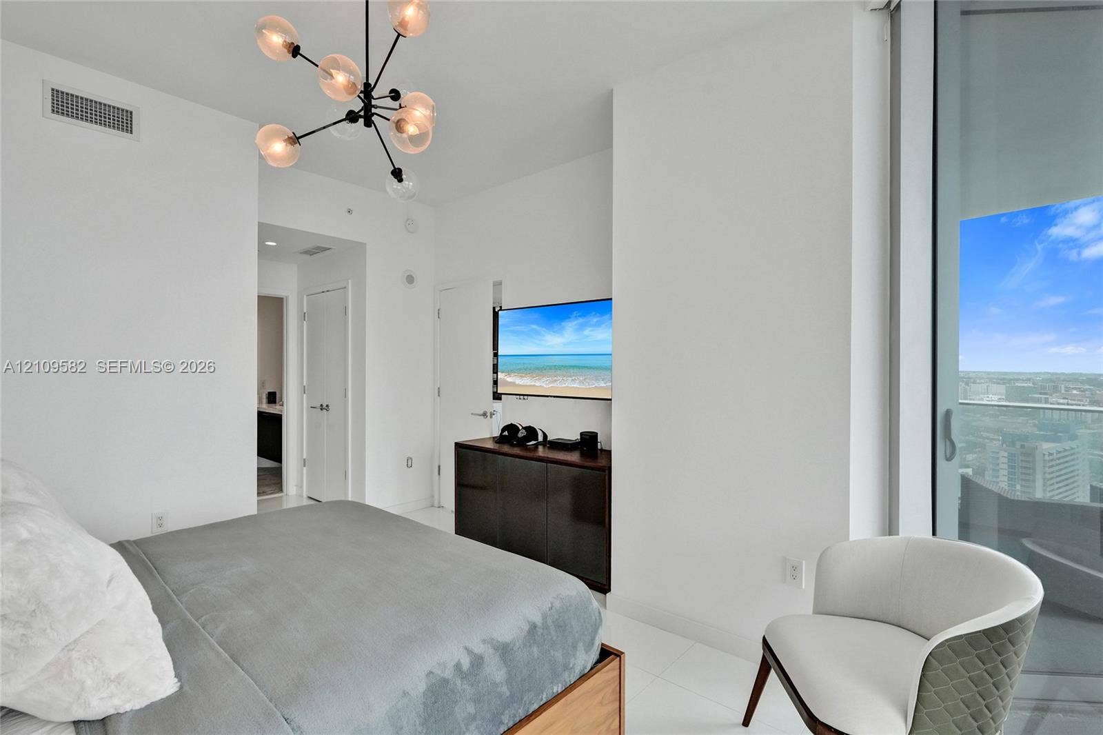 Modern bedroom featuring floor-to-ceiling glass sliding doors, polished tile flooring, a multi-arm sputnik chandelier, and neutral white wall finishes