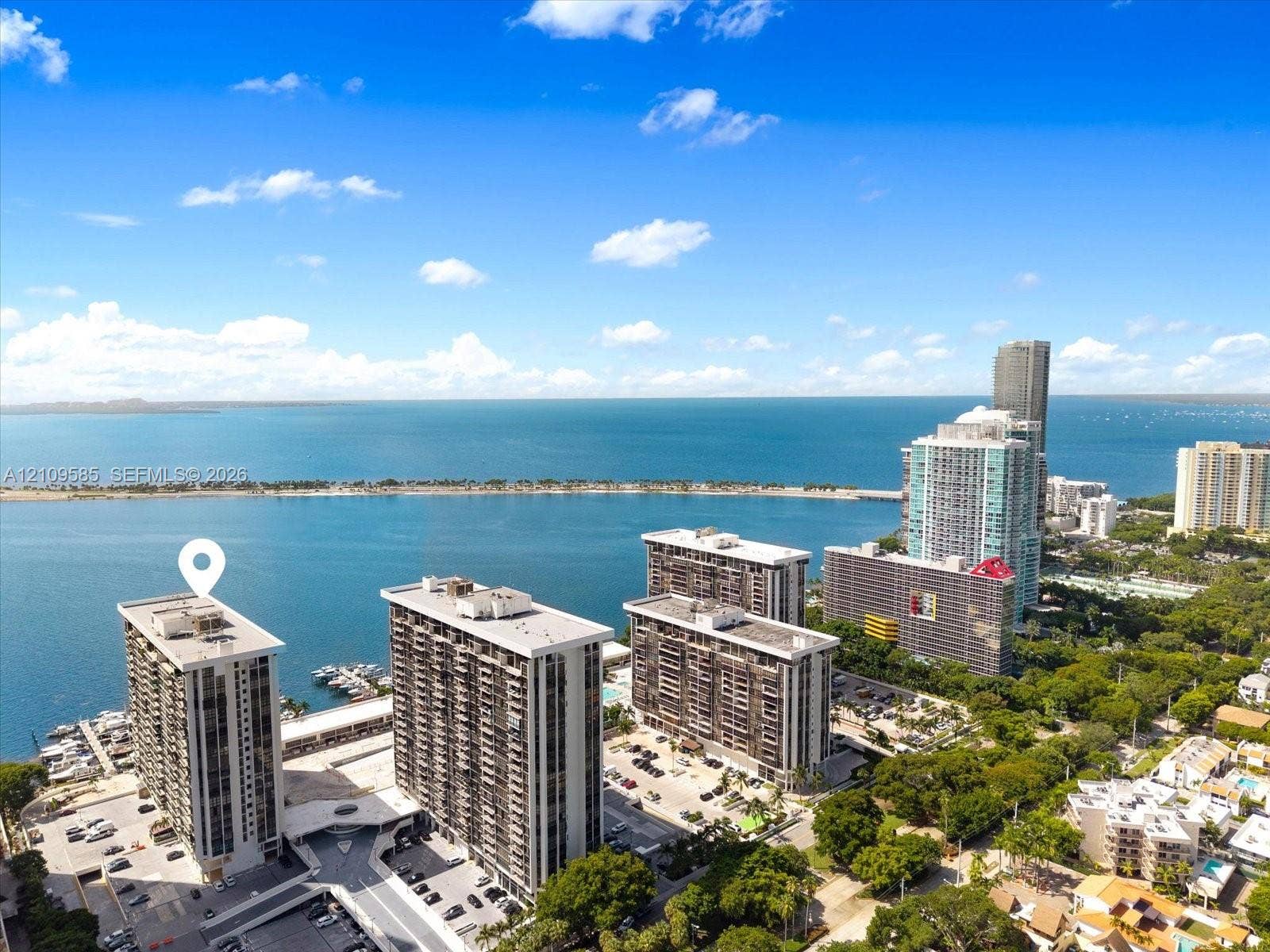 1865 Brickell Avenue, #APHVII, Miami, FL 33129 High-rise residential building featuring expansive waterfront access, an attached deep-water boat slip, and surrounding mature tree canopy