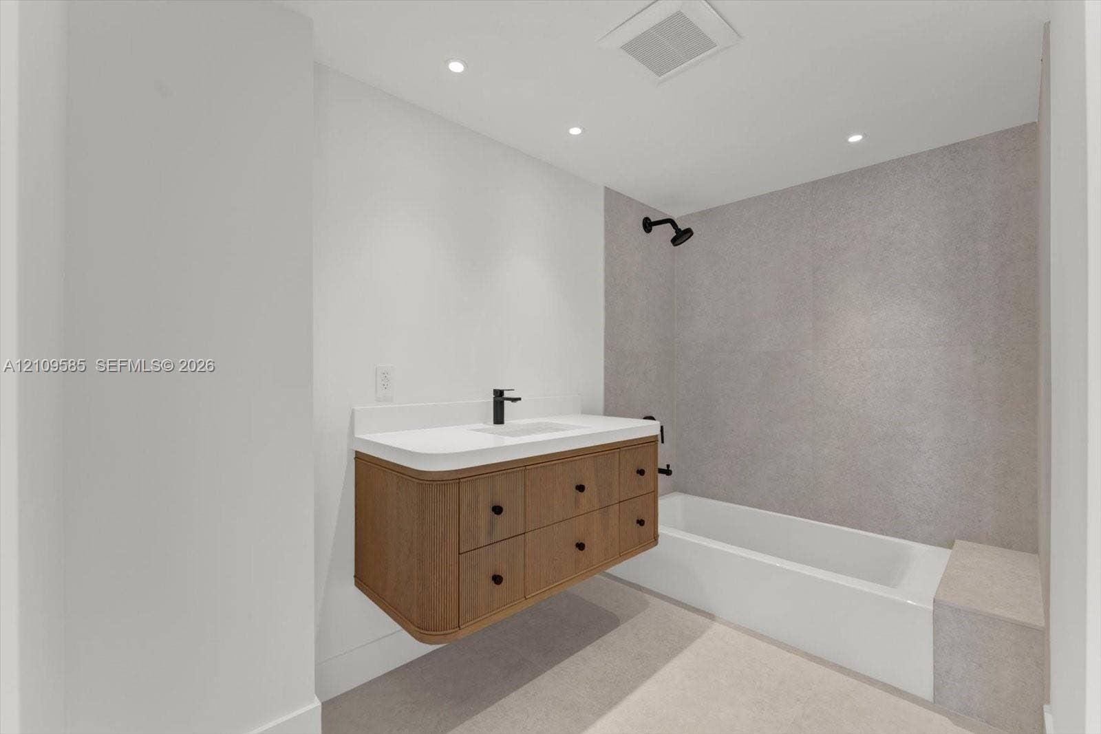 1865 Brickell Avenue, #APHVII, Miami, FL 33129 Floating wood-finish vanity with a white countertop and rectangular undermount sink, matte black faucet and shower fixtures, built-in bathtub with a stone-finish tiled surround, and recessed ceiling lighting