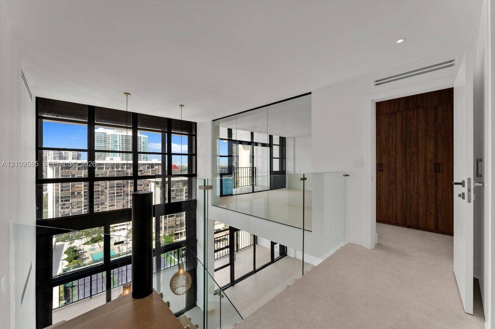 1865 Brickell Avenue, #APHVII, Miami, FL 33129 Floor-to-ceiling multi-pane windows, glass-panel railings, wood-finish cabinetry, and neutral carpeting
