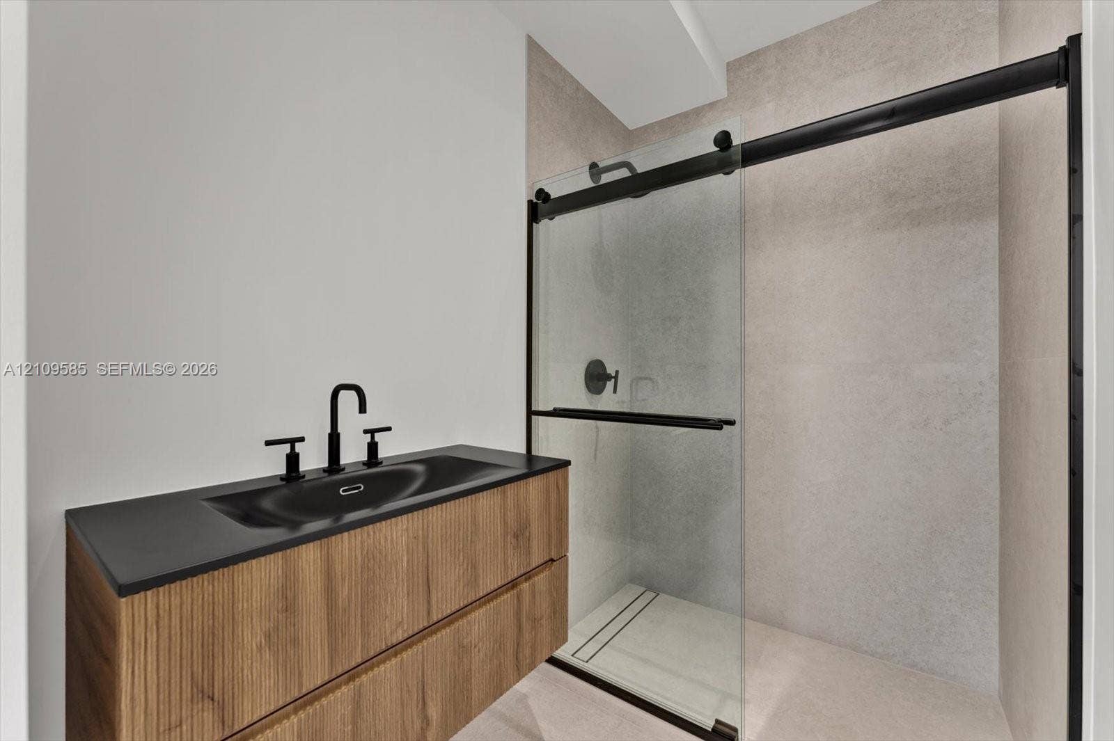 1865 Brickell Avenue, #APHVII, Miami, FL 33129 Floating wood-finish vanity with a dark countertop and integrated sink, matte black faucet, glass-enclosed shower with a sliding matte black track, and large-format wall tiling