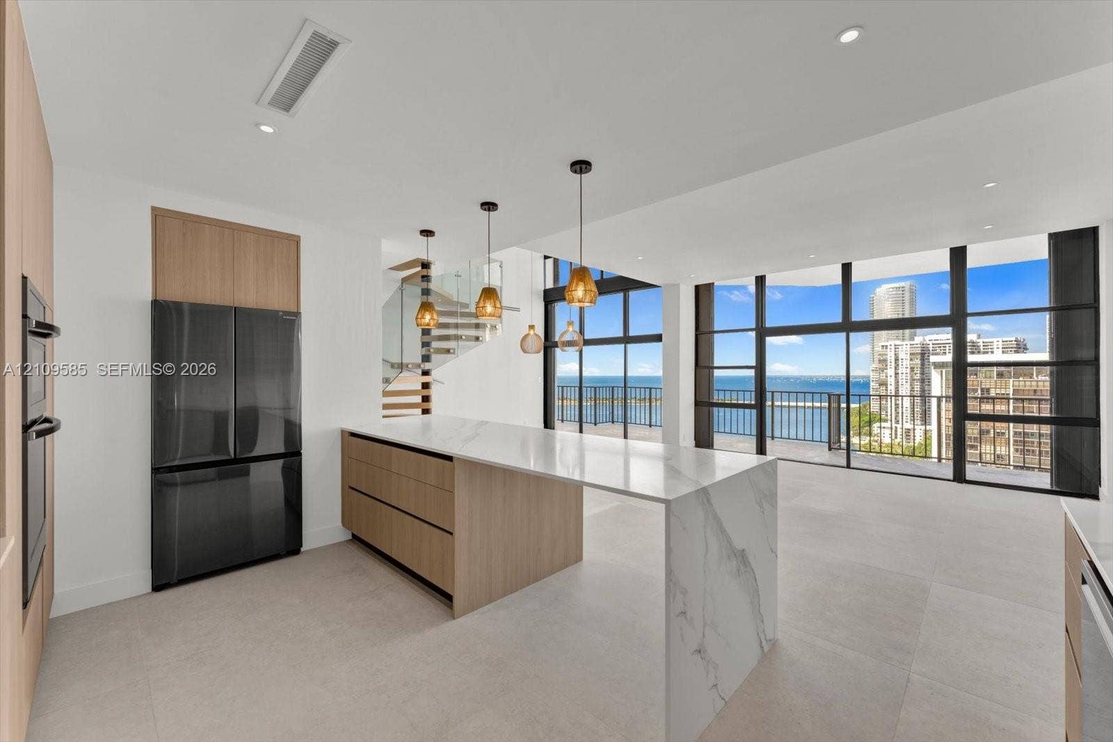 1865 Brickell Avenue, #APHVII, Miami, FL 33129 Kitchen featuring a waterfall-edge island with stone-finish countertops, flat-panel wood-finish cabinetry, floor-to-ceiling glass paneling, and pendant lighting