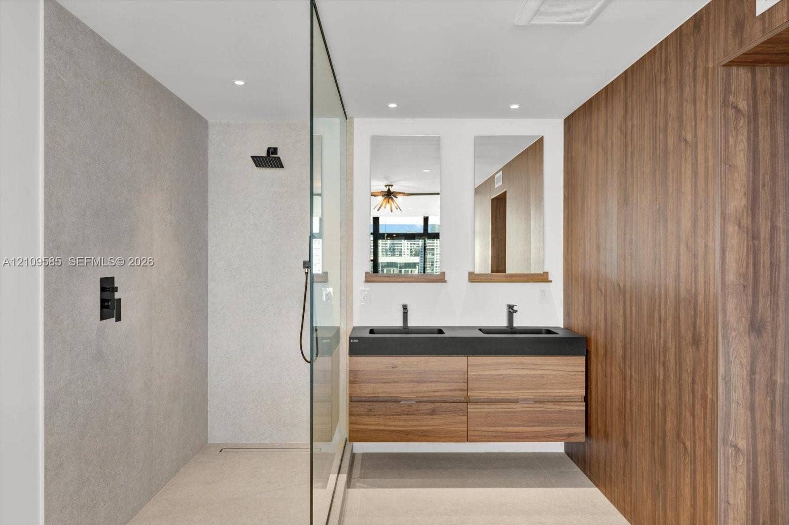 1865 Brickell Avenue, #APHVII, Miami, FL 33129 Floating wood-finish double vanity with matte black fixtures, stone-style shower surround, glass shower enclosure, and wood-finish accent wall