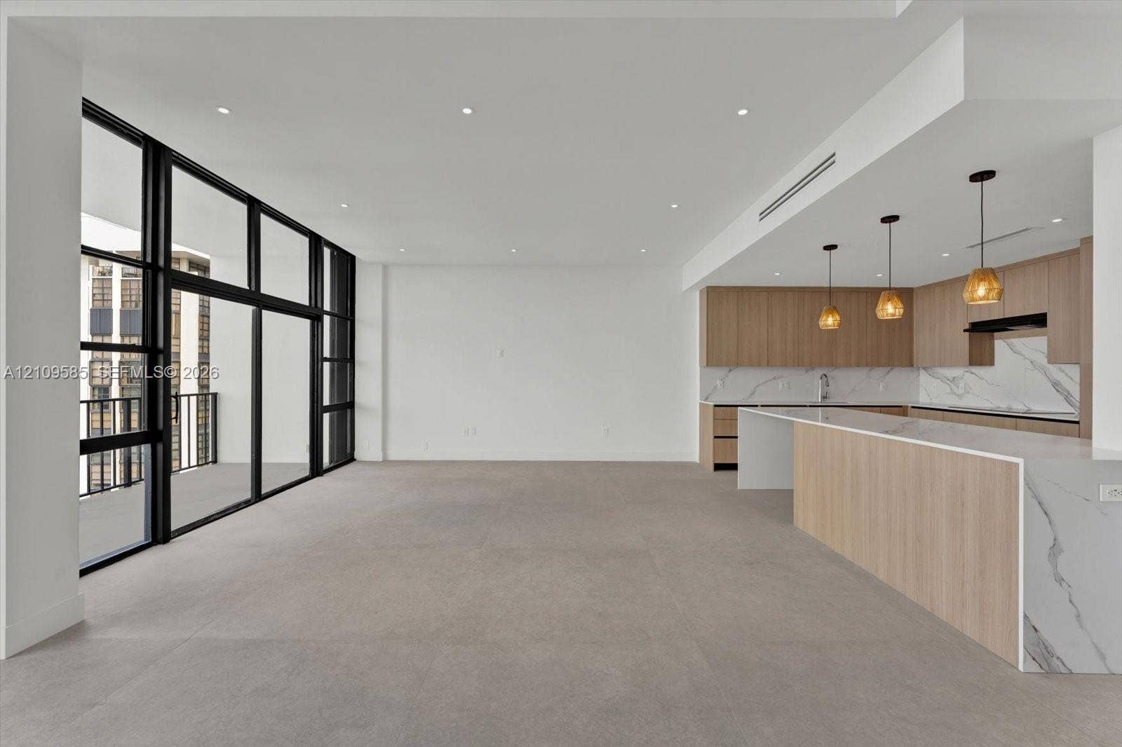 1865 Brickell Avenue, #APHVII, Miami, FL 33129 Open-concept interior featuring floor-to-ceiling black-framed glass panels, custom wood-finish cabinetry, waterfall-edge stone countertop, stone slab backsplash, and recessed lighting