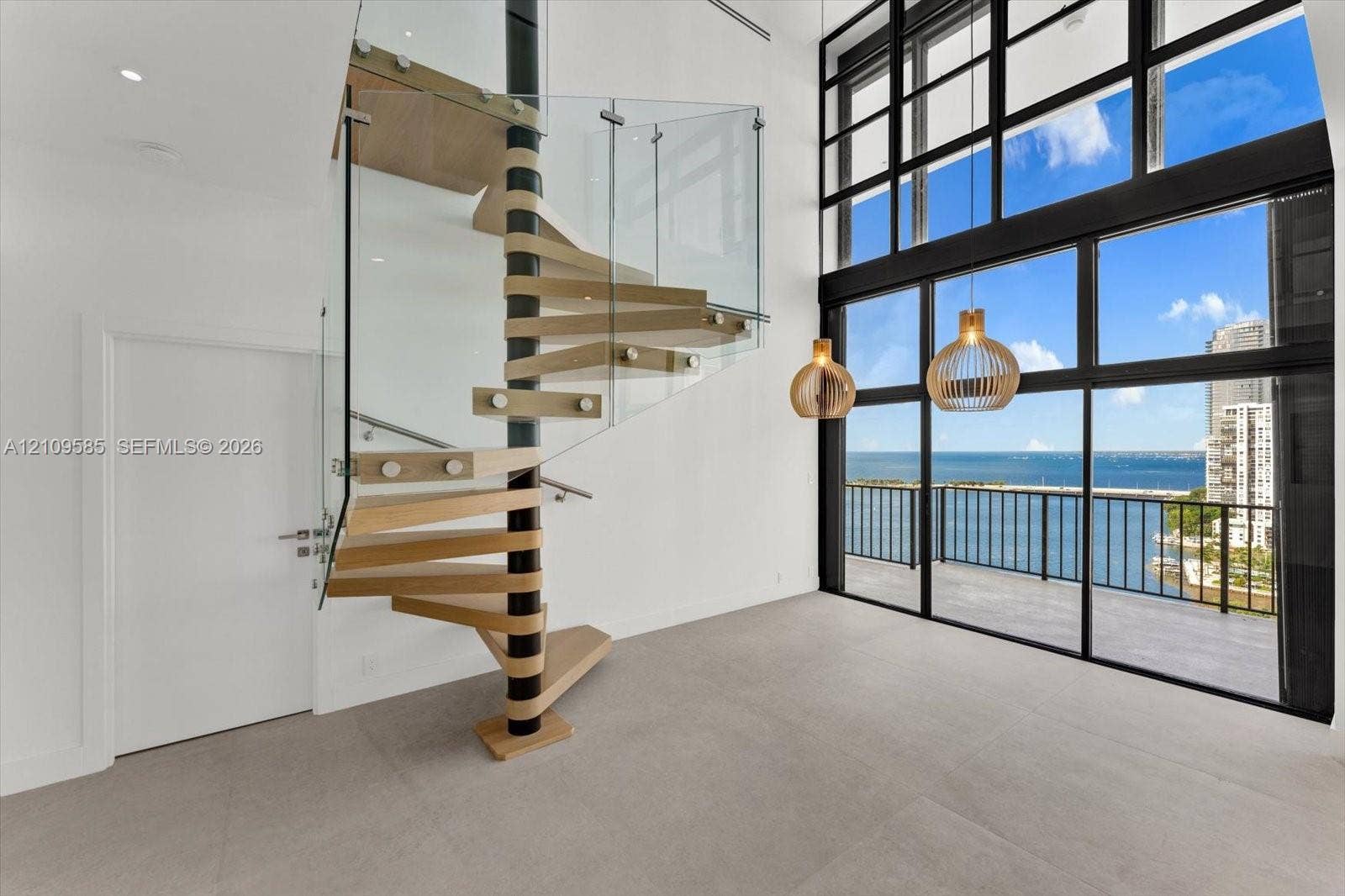 1865 Brickell Avenue, #APHVII, Miami, FL 33129 Architectural spiral staircase featuring wood-finish treads and a glass balustrade, floor-to-ceiling multi-panel windows, and pendant light fixtures