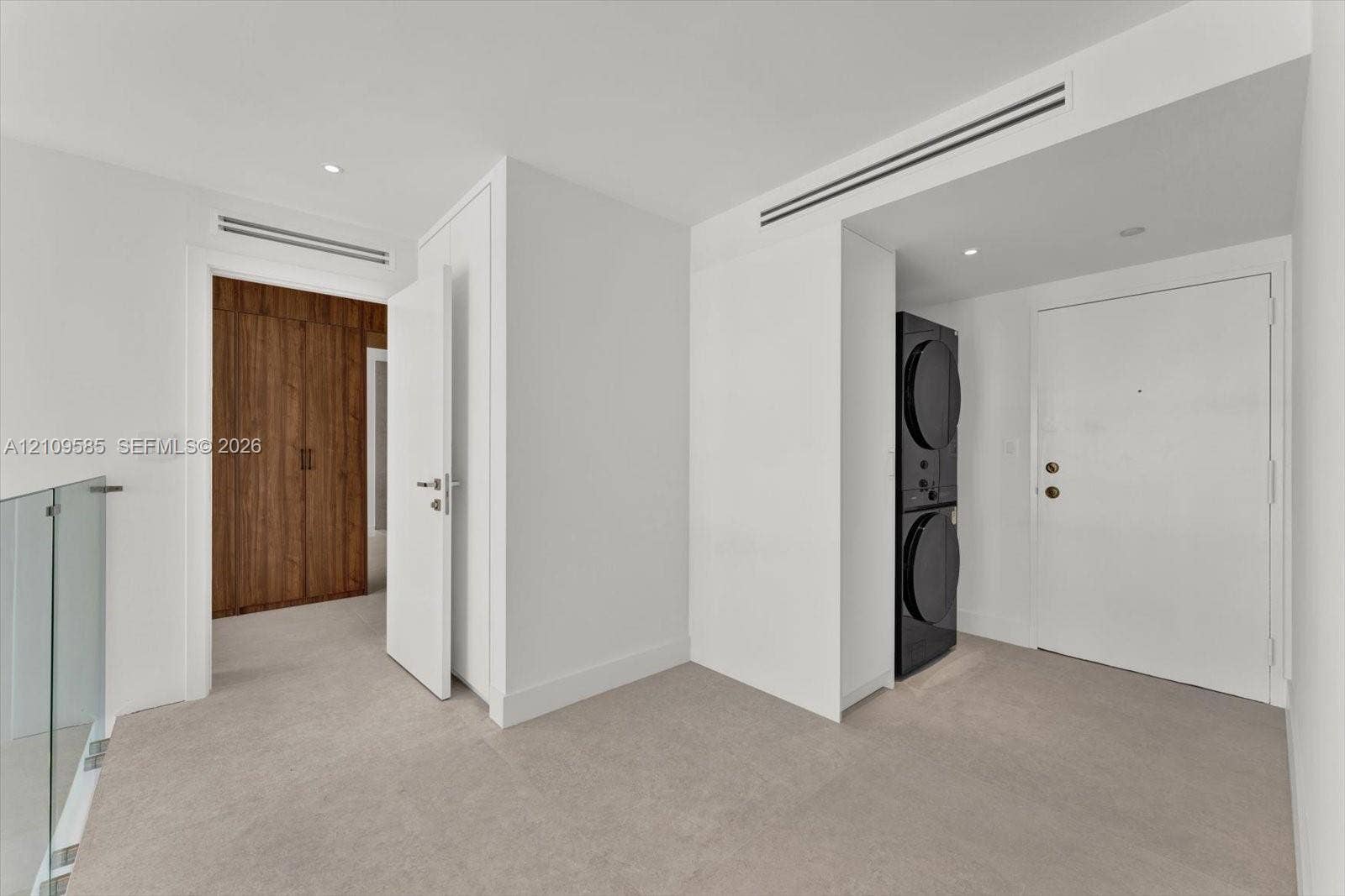 1865 Brickell Avenue, #APHVII, Miami, FL 33129 Stacked laundry unit, full-height wood-finish cabinetry, recessed ceiling lighting, and glass panel railing