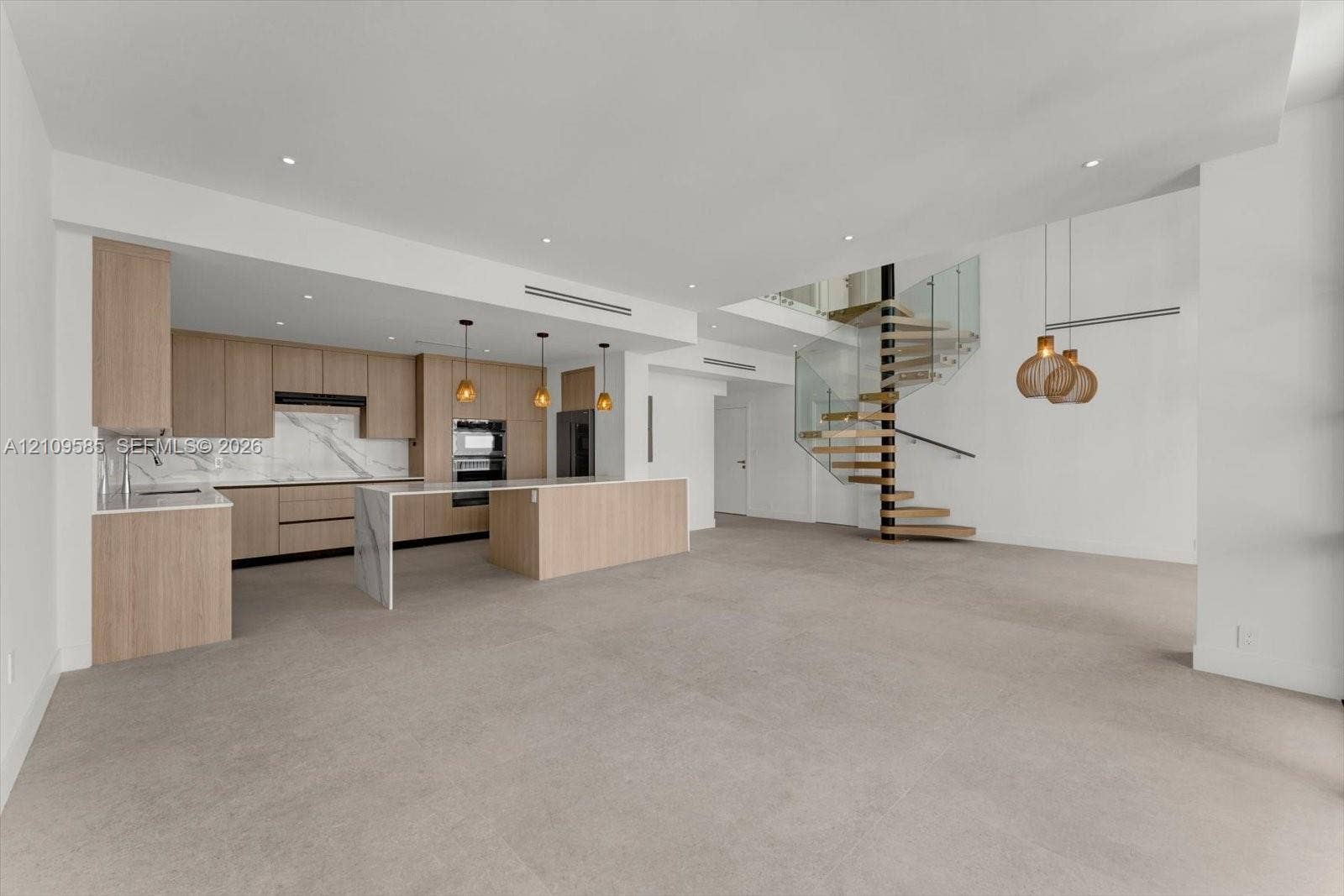 1865 Brickell Avenue, #APHVII, Miami, FL 33129 Open-concept interior featuring light wood-finish cabinetry, waterfall-edge stone island, spiral staircase with glass railing, and recessed ceiling lighting