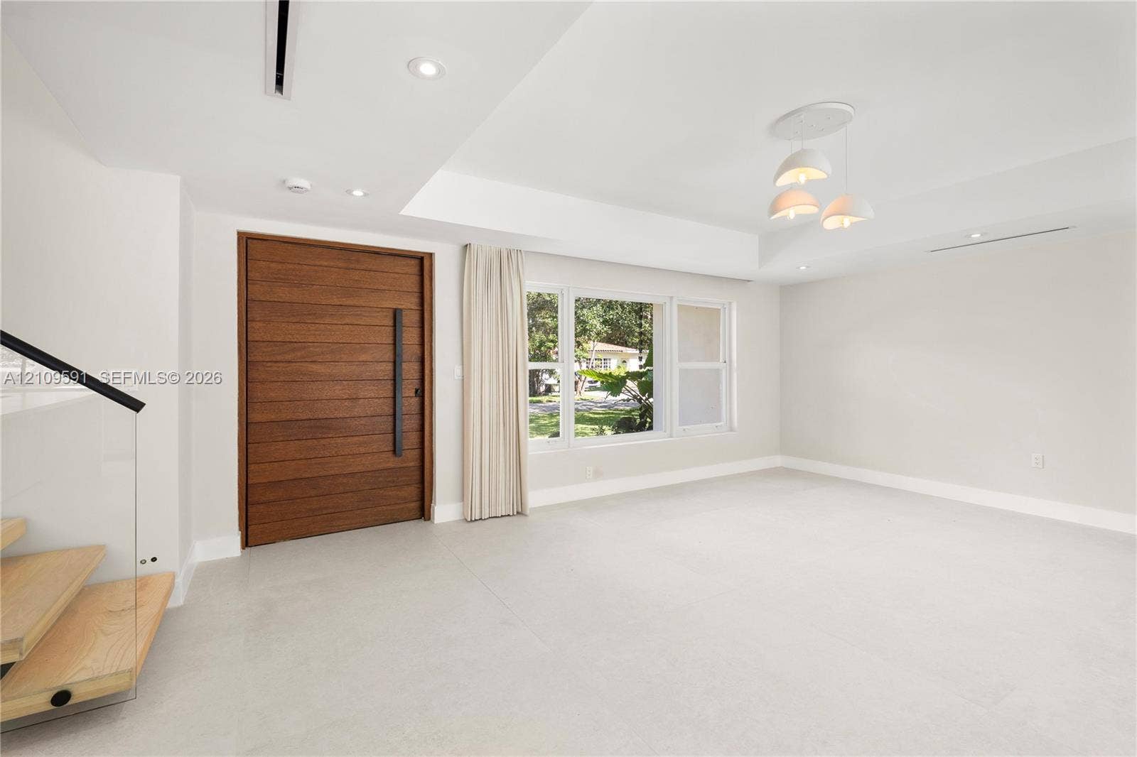 864 NE 91st Terrace, Miami Shores, FL 33138 Horizontal wood-plank entry door with a vertical matte black pull handle, recessed ceiling lighting, three-globe pendant fixture, and glass-panel staircase railing