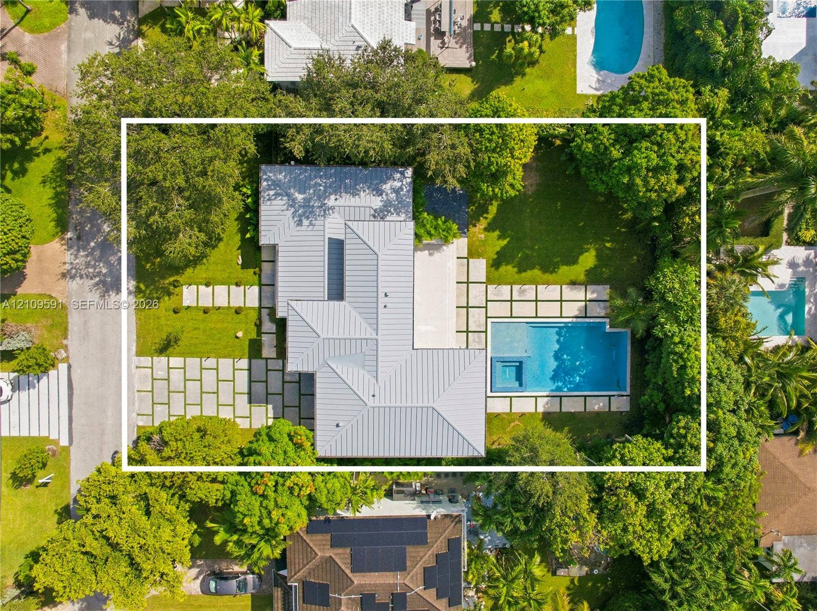 864 NE 91st Terrace, Miami Shores, FL 33138 Aerial view of residential property featuring a metal roof, swimming pool with integrated spa, concrete paver hardscaping, and mature landscaping