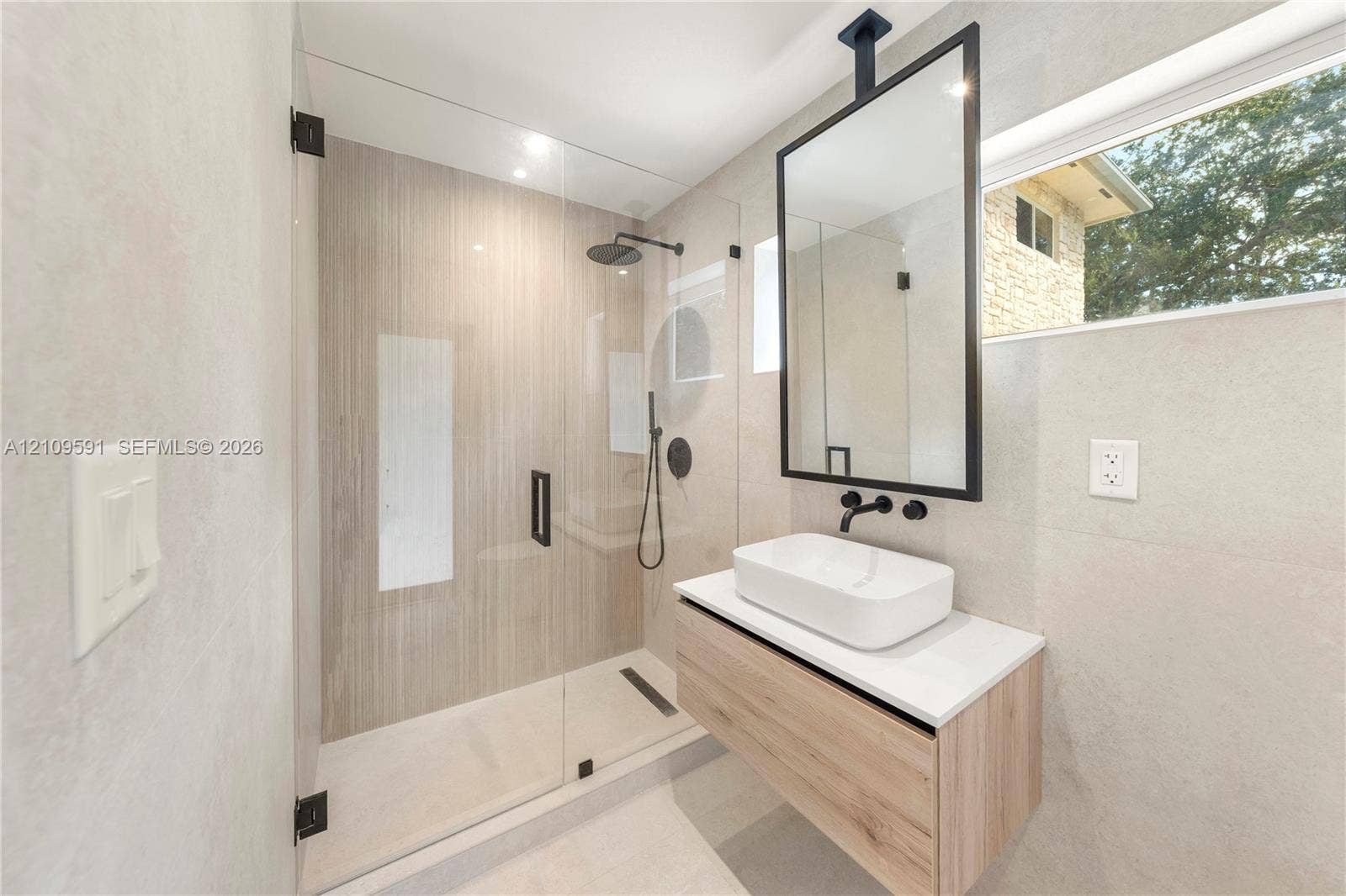 864 NE 91st Terrace, Miami Shores, FL 33138 Cabana Bath Floating vanity with rectangular vessel sink and countertop, ceiling-mounted mirror with black frame, walk-in shower with frameless glass enclosure, and matte black plumbing fixtures