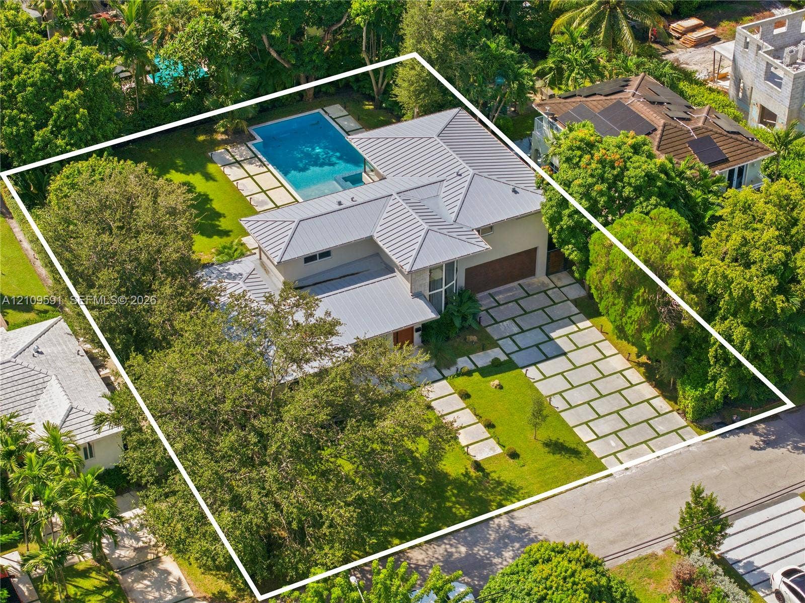 864 NE 91st Terrace, Miami Shores, FL 33138 Metal roof residence featuring a swimming pool, paved hardscaping, multi-car garage, and established landscaping