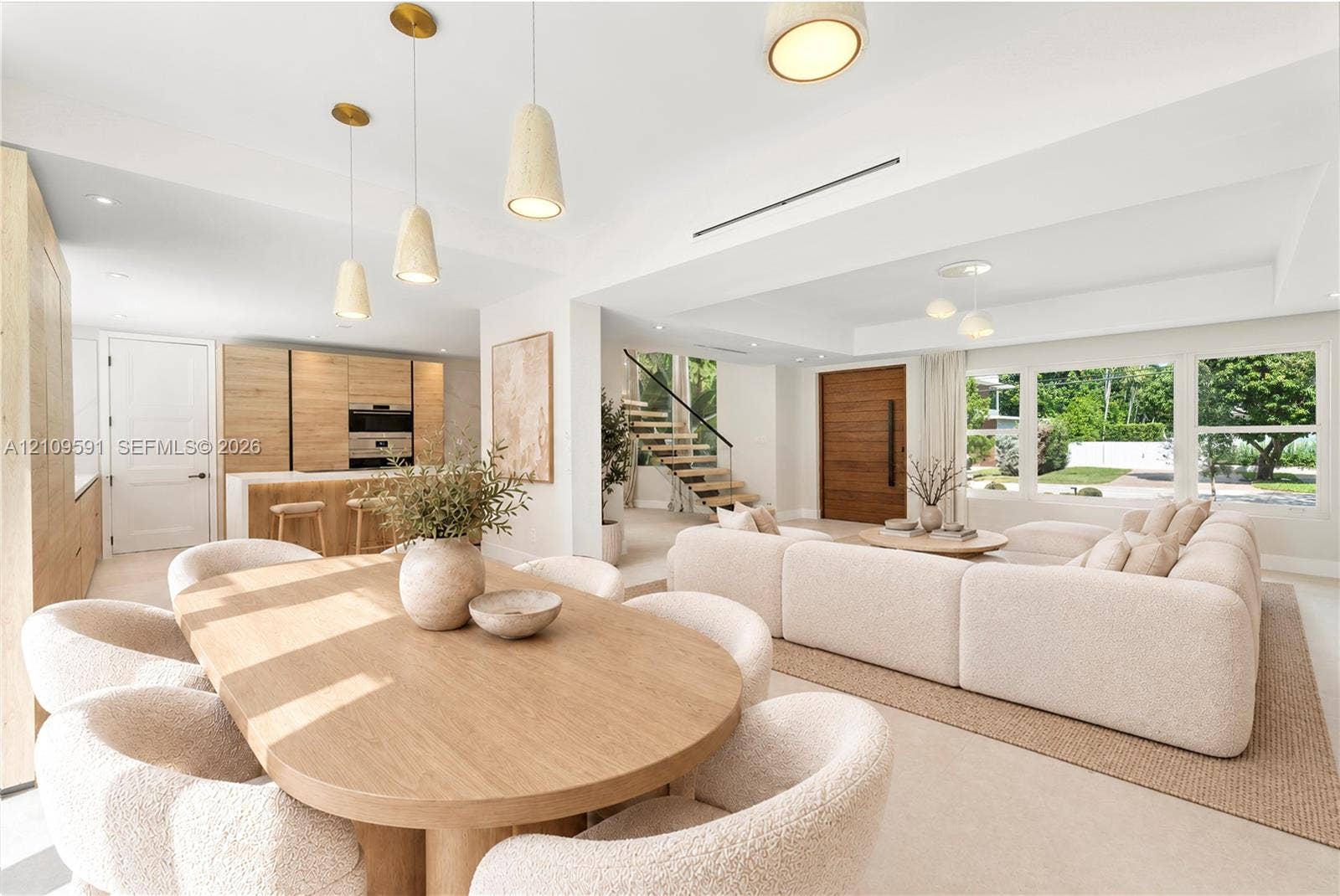 864 NE 91st Terrace, Miami Shores, FL 33138 Virtually Staged: Open-concept interior featuring light wood-finish cabinetry, a floating staircase with glass railing, recessed lighting, pendant fixtures, and large picture windows
