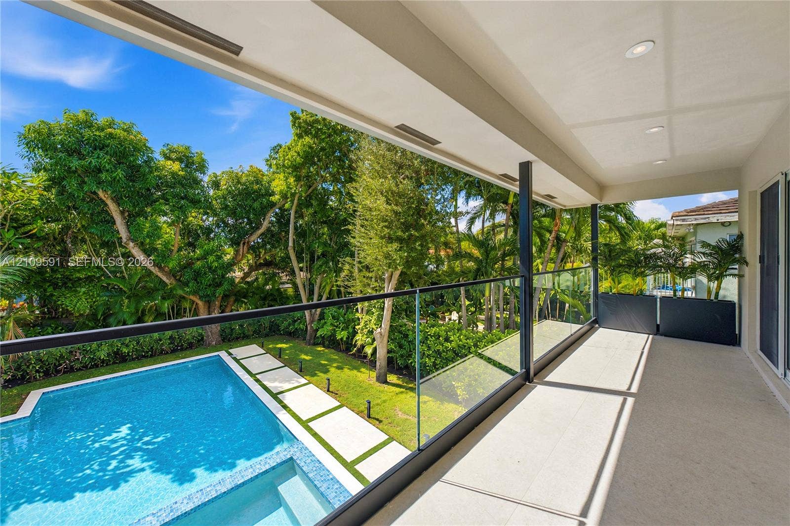 864 NE 91st Terrace, Miami Shores, FL 33138 Covered balcony featuring a frameless glass railing, recessed ceiling lighting, swimming pool with integrated spa, concrete paver path, and mature landscape