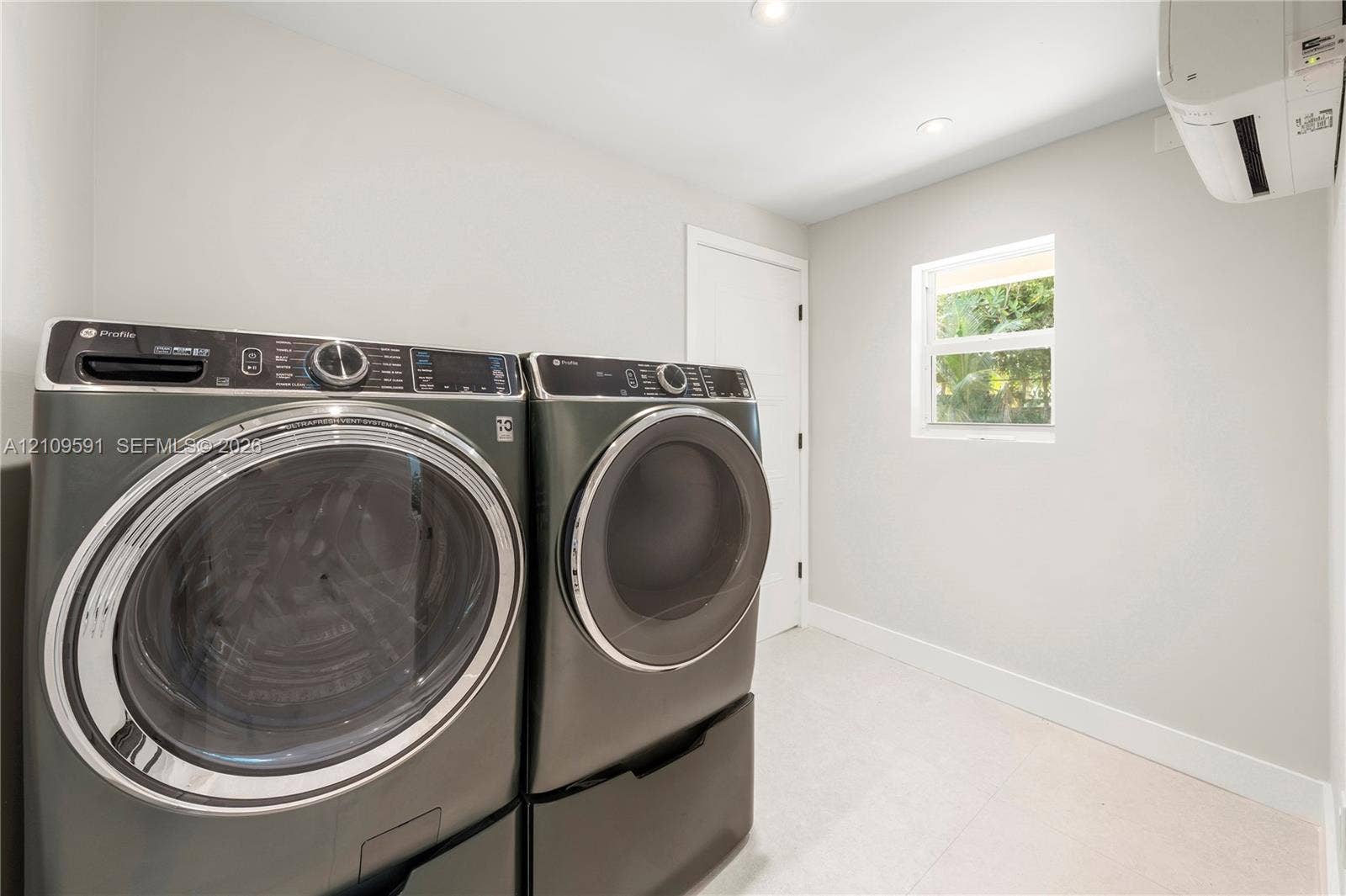 864 NE 91st Terrace, Miami Shores, FL 33138 Laundry space featuring wall-mounted ductless climate control, recessed ceiling lighting, a window, and neutral-toned flooring