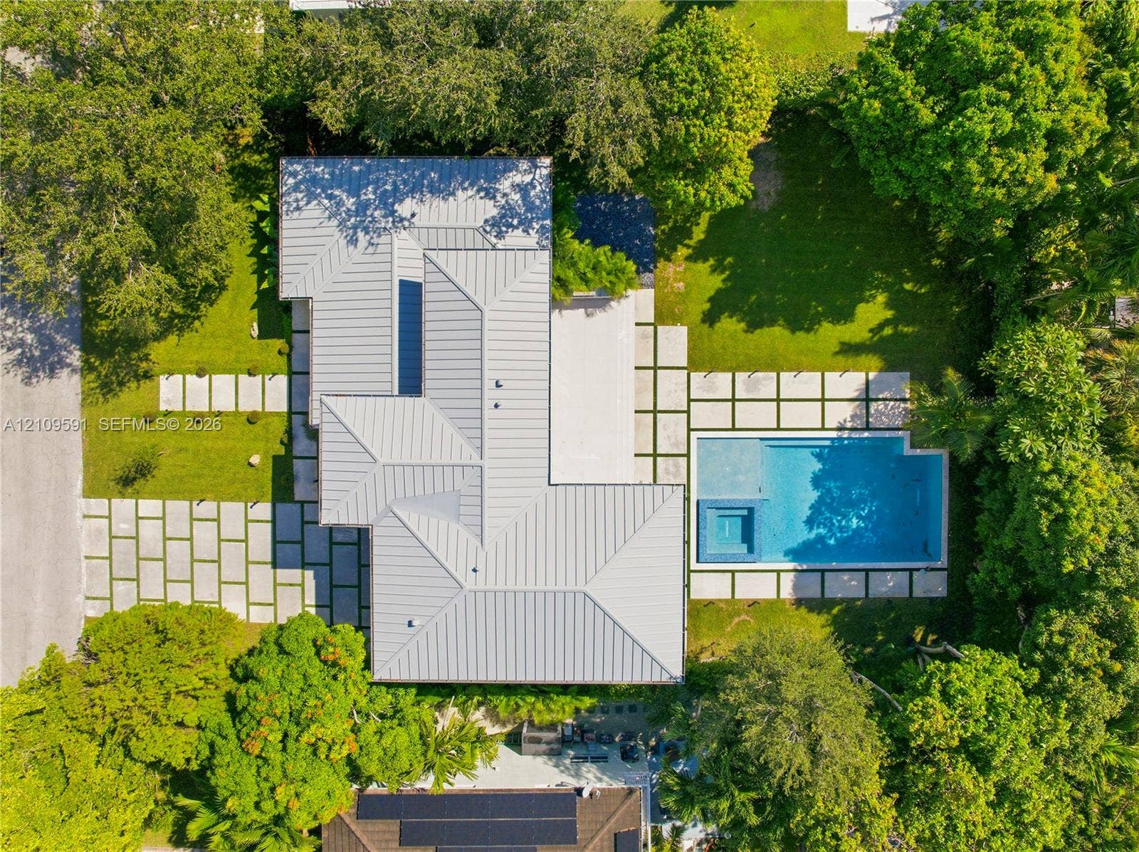 864 NE 91st Terrace, Miami Shores, FL 33138 Aerial perspective of a property featuring a standing seam metal roof, geometric concrete paver hardscaping, an in-ground swimming pool with an integrated spa, and mature perimeter landscaping