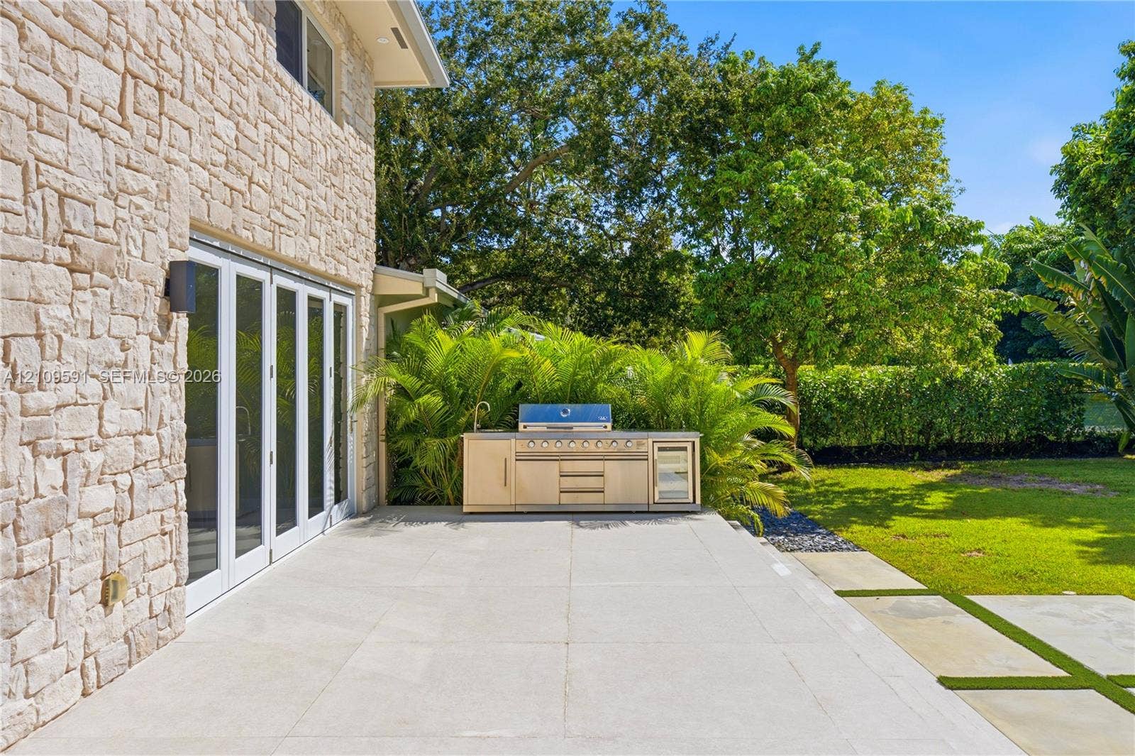 864 NE 91st Terrace, Miami Shores, FL 33138 Outdoor terrace featuring a stacked stone exterior, large-format stone pavers, and a built-in stainless steel kitchen with a grill and integrated refrigeration
