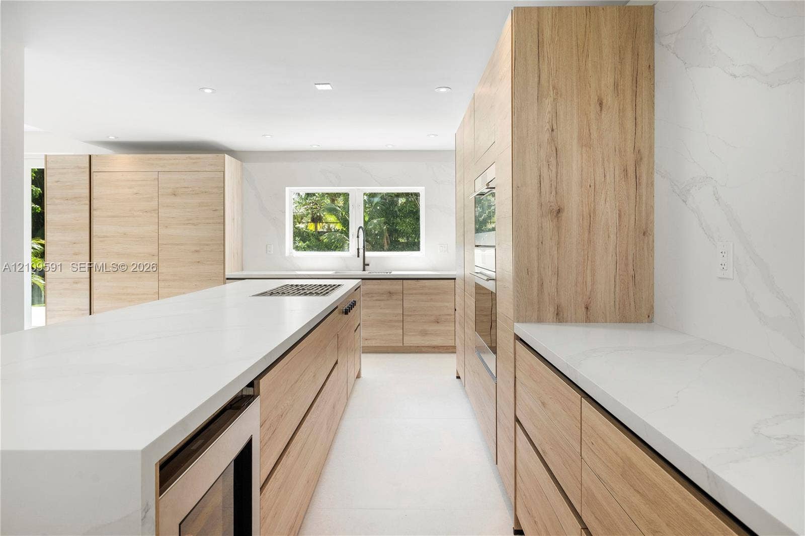864 NE 91st Terrace, Miami Shores, FL 33138 Kitchen featuring light wood-finish cabinetry, quartz countertops with full-height backsplash, a large center island, built-in stainless steel appliances, and recessed lighting