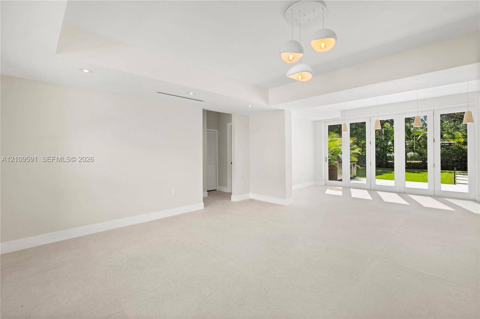 864 NE 91st Terrace, Miami Shores, FL 33138 Large-format tile flooring, tray ceilings with recessed lighting, multi-globe pendant light fixture, and floor-to-ceiling glass panel doors