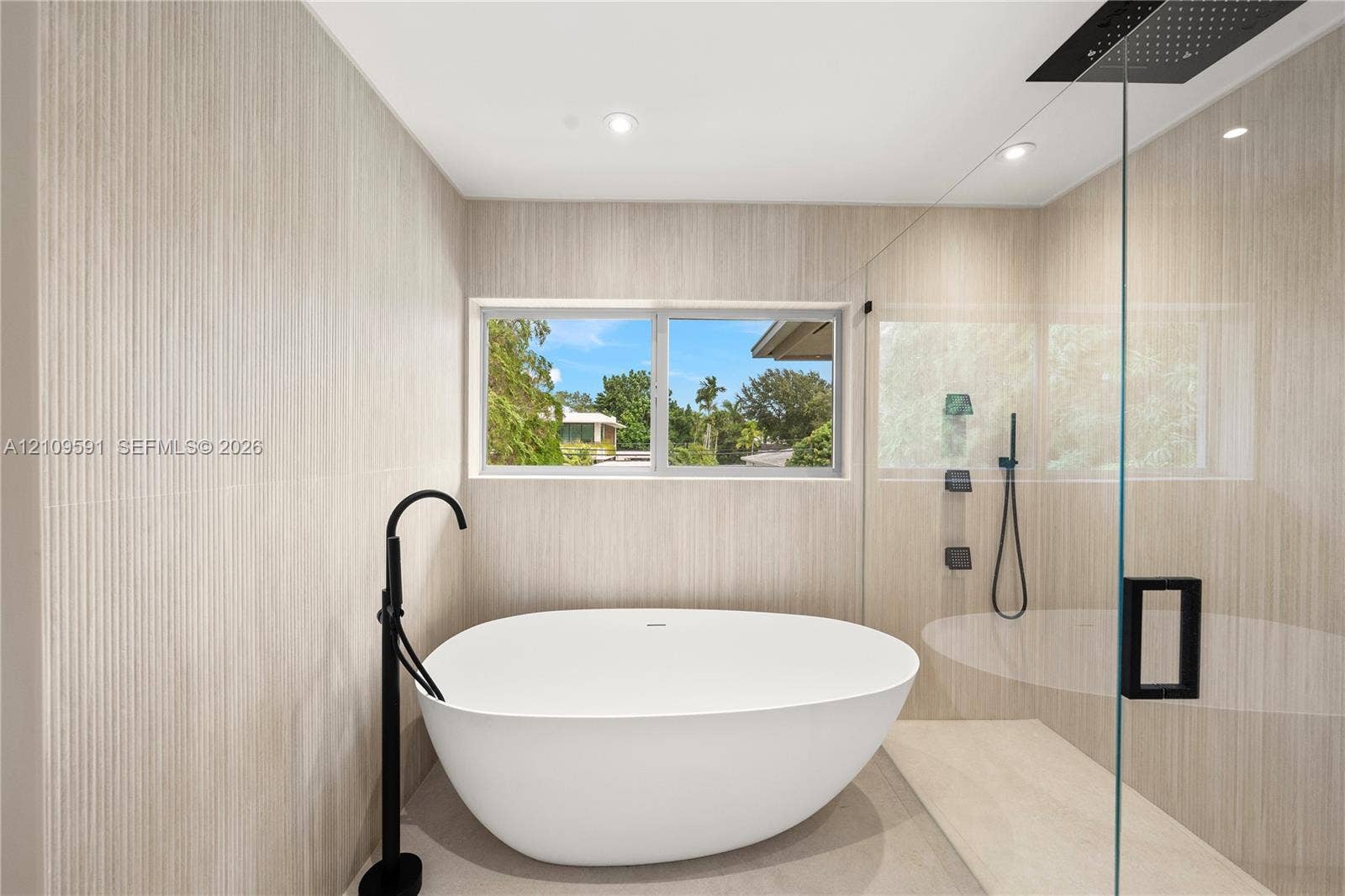 864 NE 91st Terrace, Miami Shores, FL 33138 Freestanding soaking tub with matte black floor-mounted faucet, walk-in shower with glass enclosure, rain shower head, and floor-to-ceiling textured tile walls