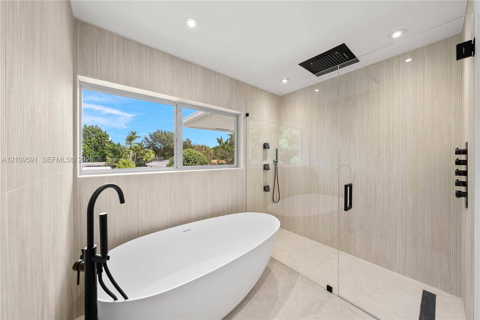 864 NE 91st Terrace, Miami Shores, FL 33138 Freestanding soaking tub with matte black floor-mounted faucet, walk-in shower with frameless glass enclosure, rainfall showerhead, and neutral wall tile