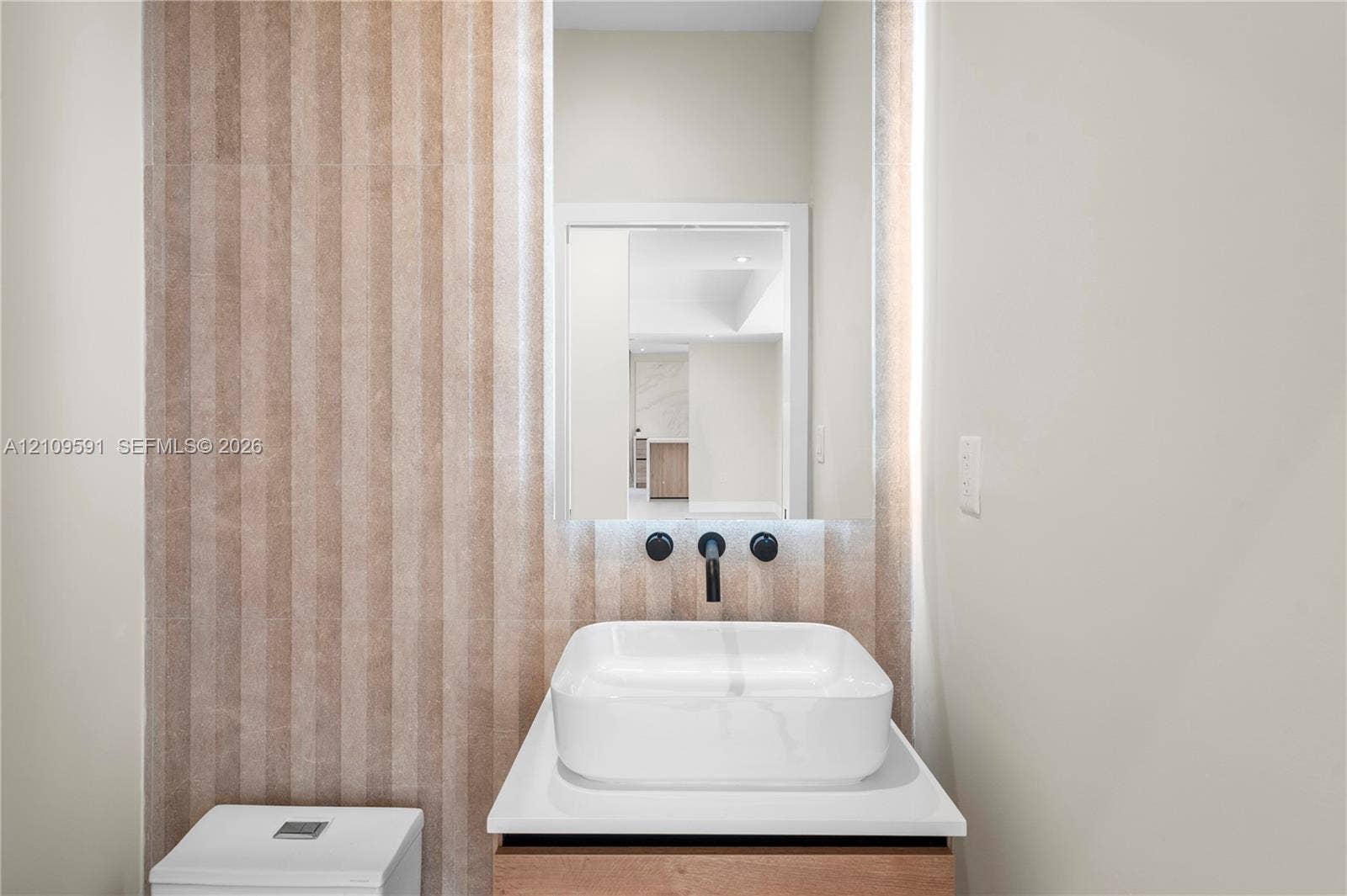 864 NE 91st Terrace, Miami Shores, FL 33138 Half Bath off living room. Wall-mounted matte black faucet, white rectangular vessel sink, white countertop, wood-finish vanity, and vertical textured stone wall tile