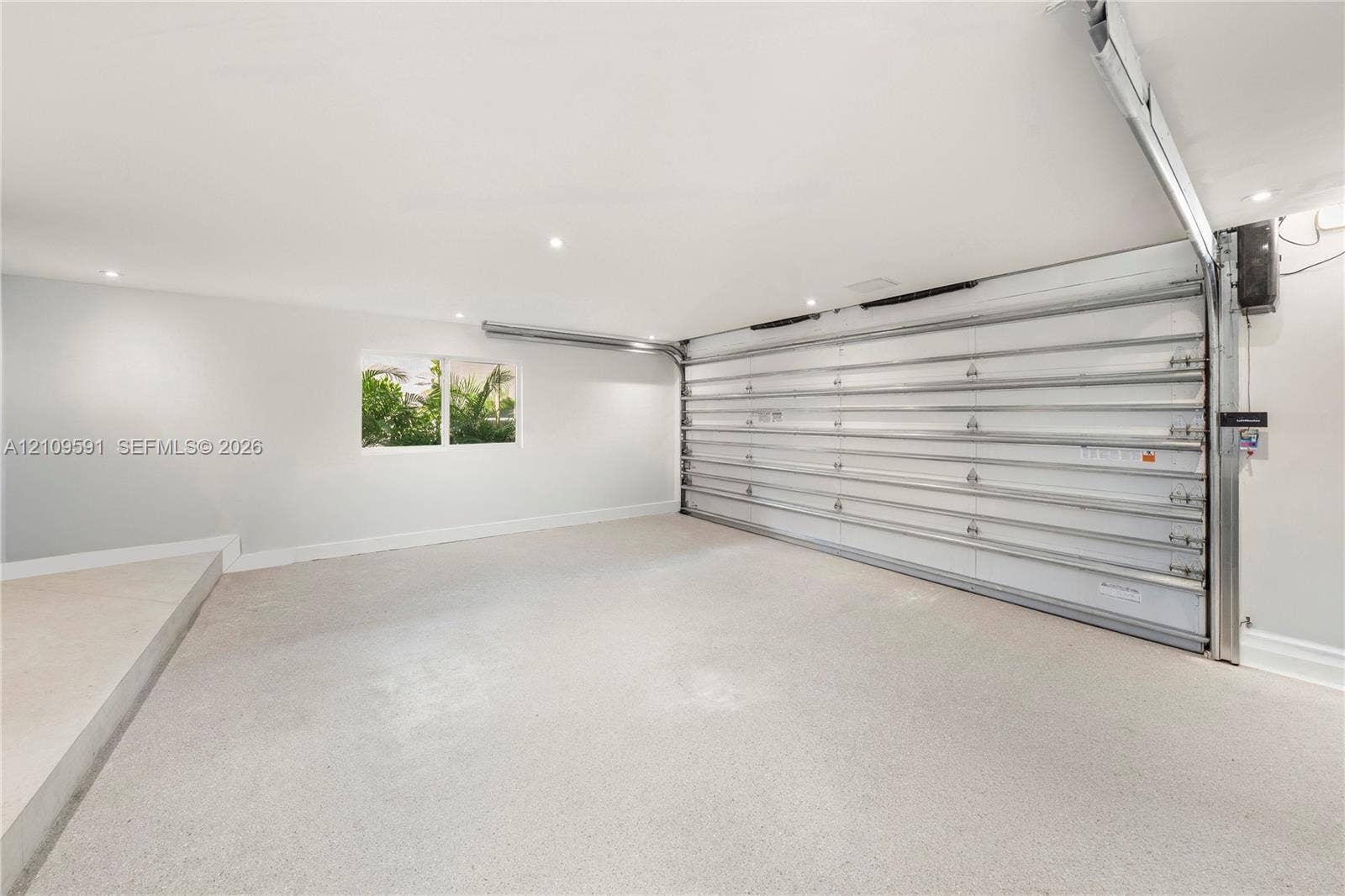 864 NE 91st Terrace, Miami Shores, FL 33138 Garage interior featuring a seamless epoxy floor finish, recessed ceiling lighting, a white sectional garage door, and a single-pane window