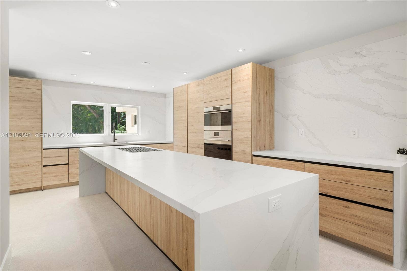 864 NE 91st Terrace, Miami Shores, FL 33138 Modern kitchen featuring light wood-finish cabinetry, a waterfall-edge center island, solid-surface countertops, and full-height stone backsplash