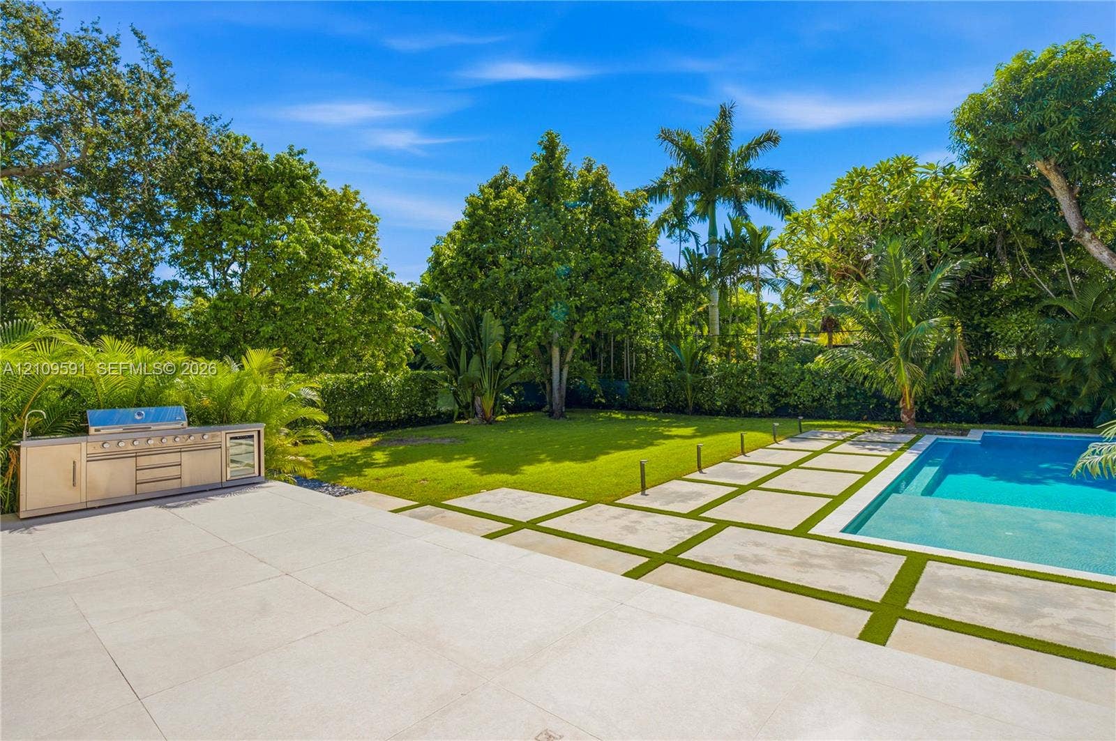 864 NE 91st Terrace, Miami Shores, FL 33138 Backyard featuring a swimming pool, integrated stainless steel outdoor kitchen, stone paver patio with turf inlays, and mature landscaping