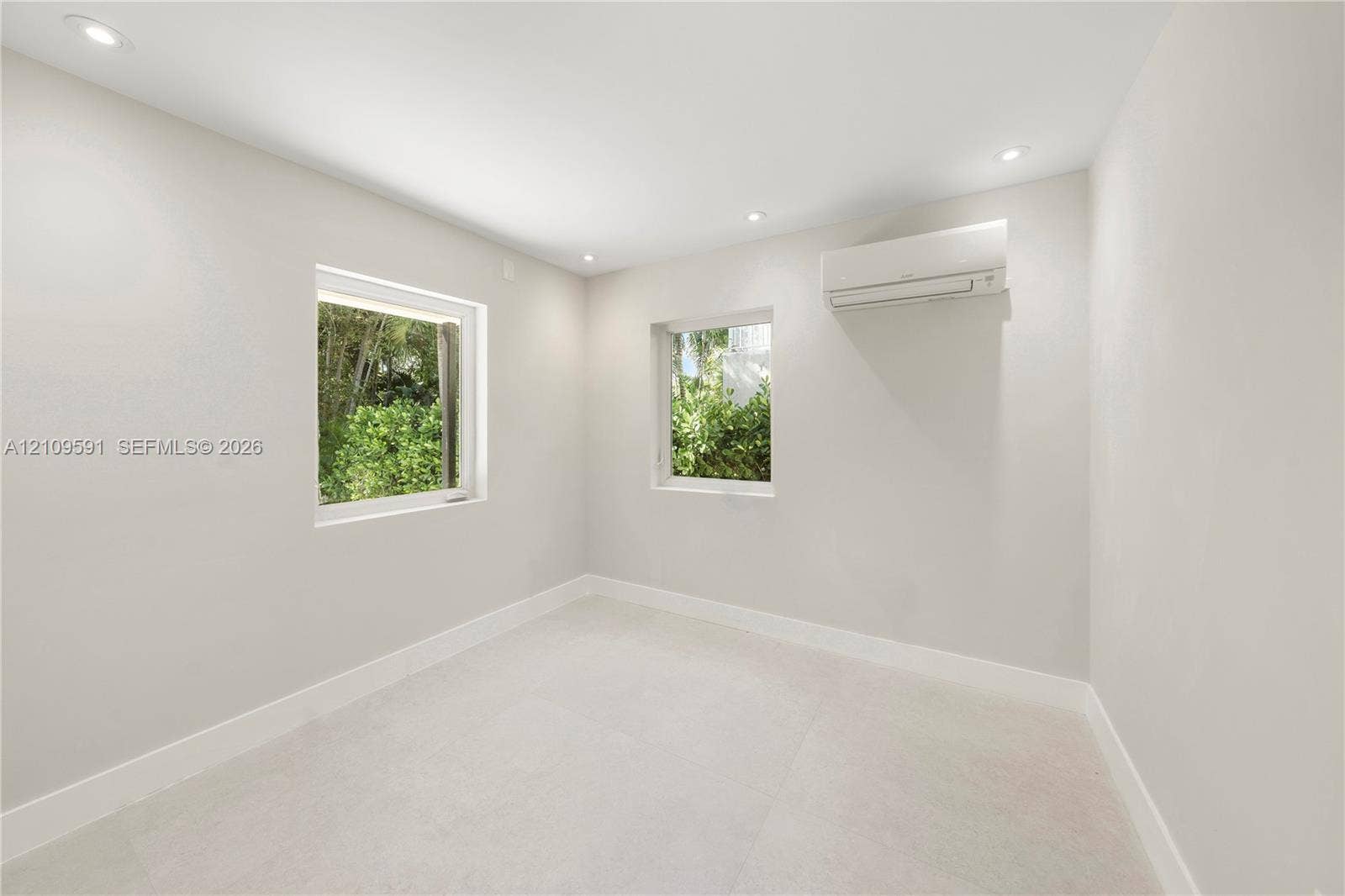 864 NE 91st Terrace, Miami Shores, FL 33138 Neutral interior space featuring recessed ceiling lighting, light-toned flooring, two windows, and a wall-mounted ductless air conditioning unit