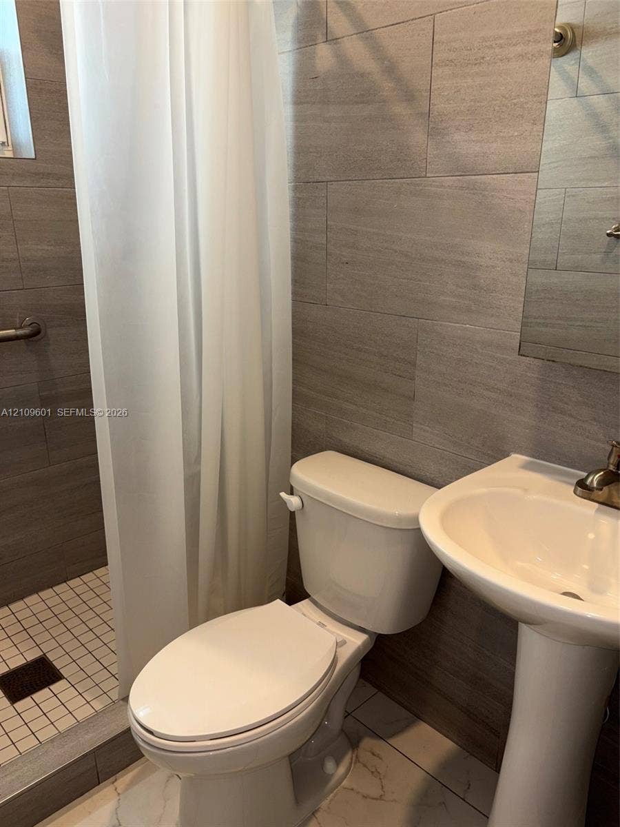 6320 Cleveland Street, Hollywood, Hollywood, FL 33024 Bathroom featuring large-format neutral wall tile, white pedestal sink with metal faucet, walk-in shower with mosaic tile flooring, and wall-mounted grab bar