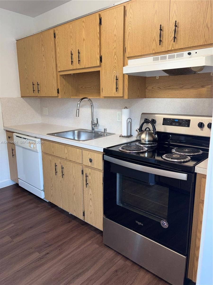 6320 Cleveland Street, Hollywood, Hollywood, FL 33024 Kitchen featuring wood cabinetry with matte black pulls, stainless steel sink with high-arc pull-down faucet, white solid-surface countertops, wood-finish flooring, and a stainless steel electric range