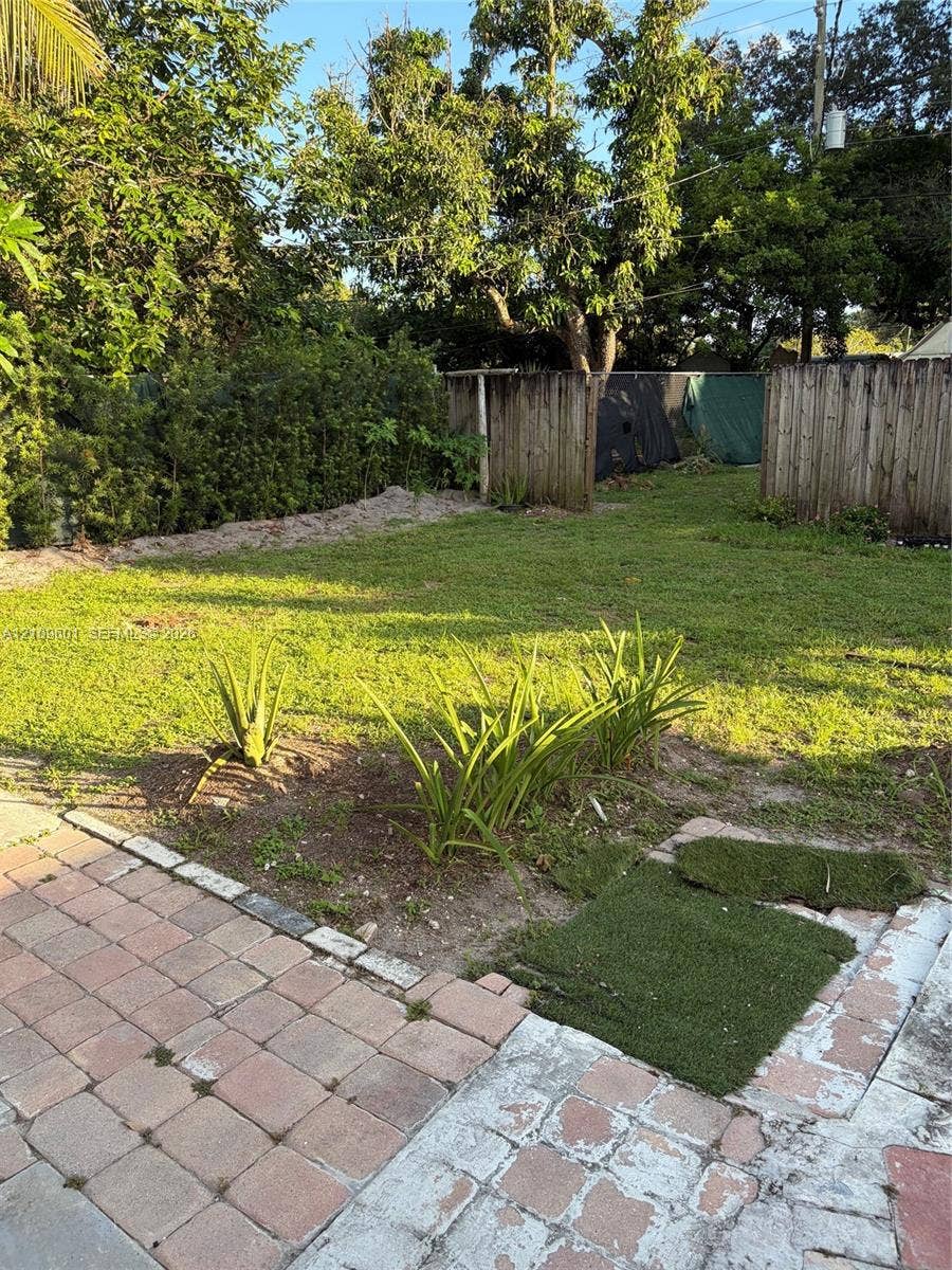 6320 Cleveland Street, Hollywood, Hollywood, FL 33024 Backyard featuring a paved brick patio, grassy lawn, mature trees, wood privacy fencing, and established ground plantings
