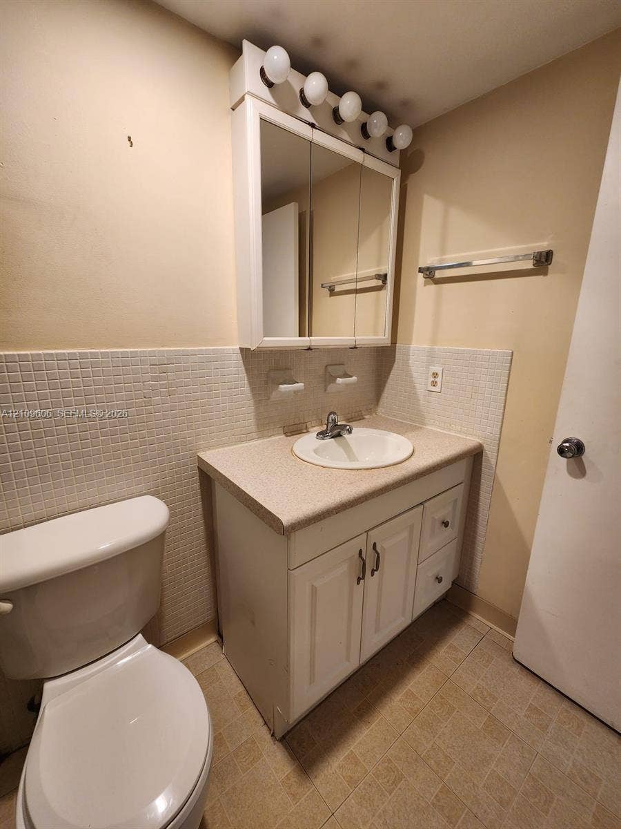 1851 NE 62nd Street, #610, Fort Lauderdale, FL 33308 Bathroom vanity featuring a solid-surface countertop, integrated basin, white cabinetry with storage drawers, tri-view medicine cabinet with integrated light fixture, and tiled backsplash