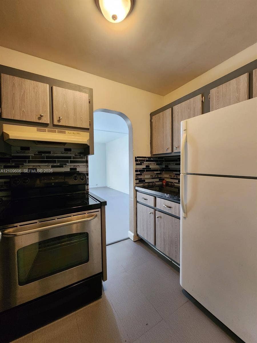 1851 NE 62nd Street, #610, Fort Lauderdale, FL 33308 Kitchen featuring wood-finish cabinetry, a stainless steel range, a dark linear-tile backsplash, and an arched doorway